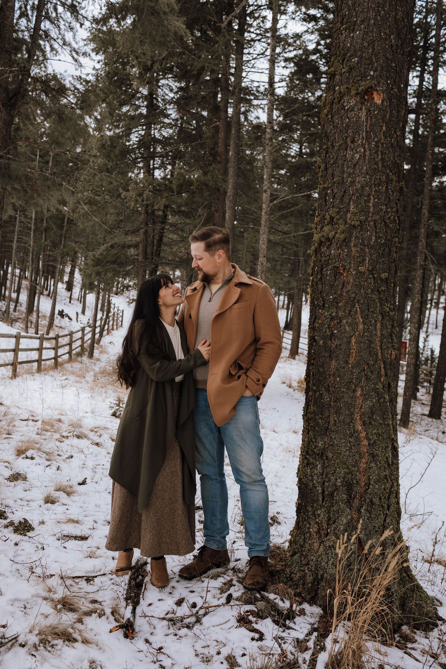 Couple in warm coats sharing intimate moment in snowy pine forest.