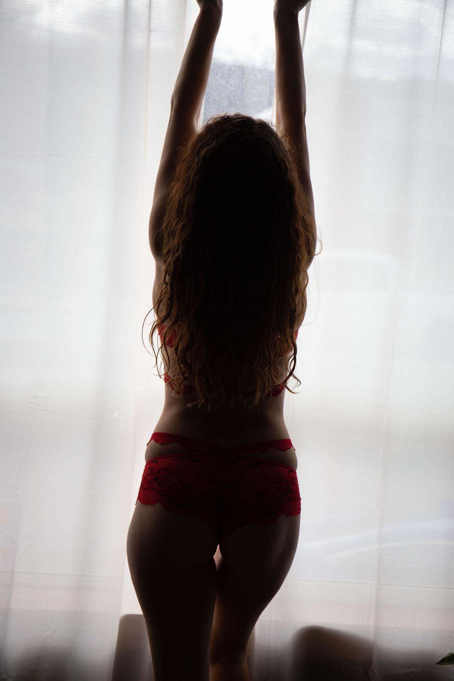 Backlit silhouette stretching arms upward against sheer curtain window.