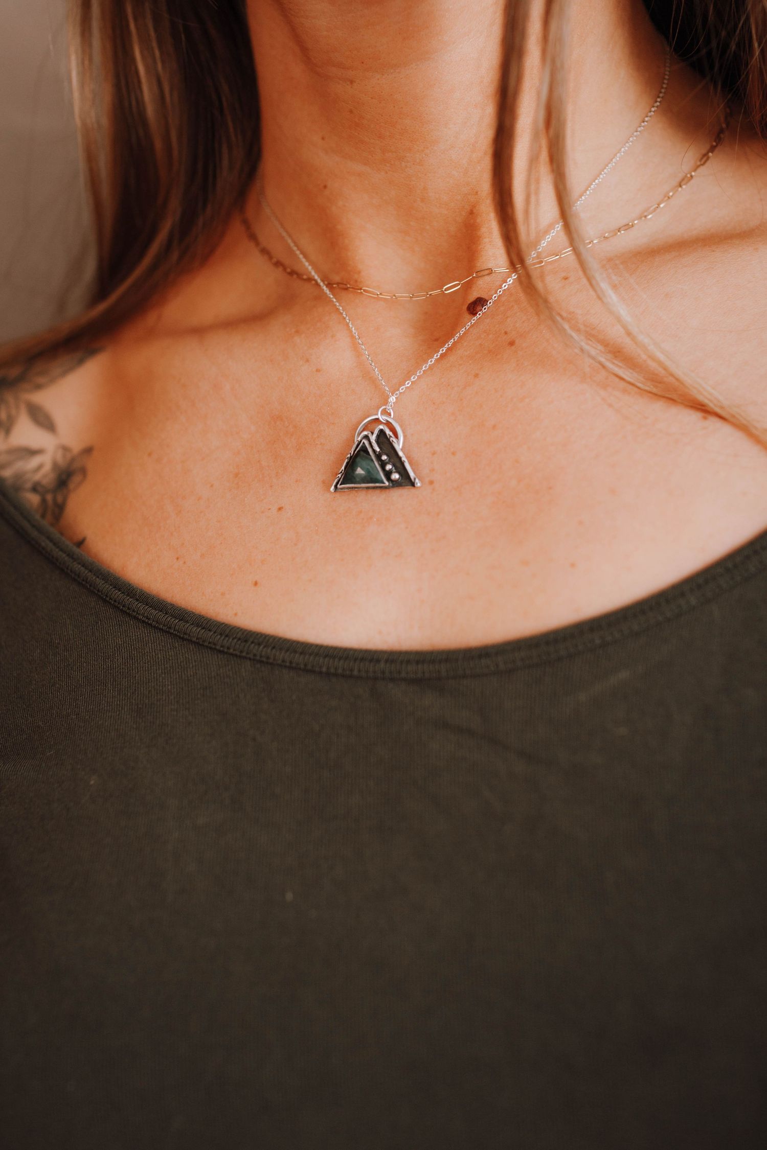 Triangular pendant necklace displayed against a dark colored top with subtle tattoo detail.