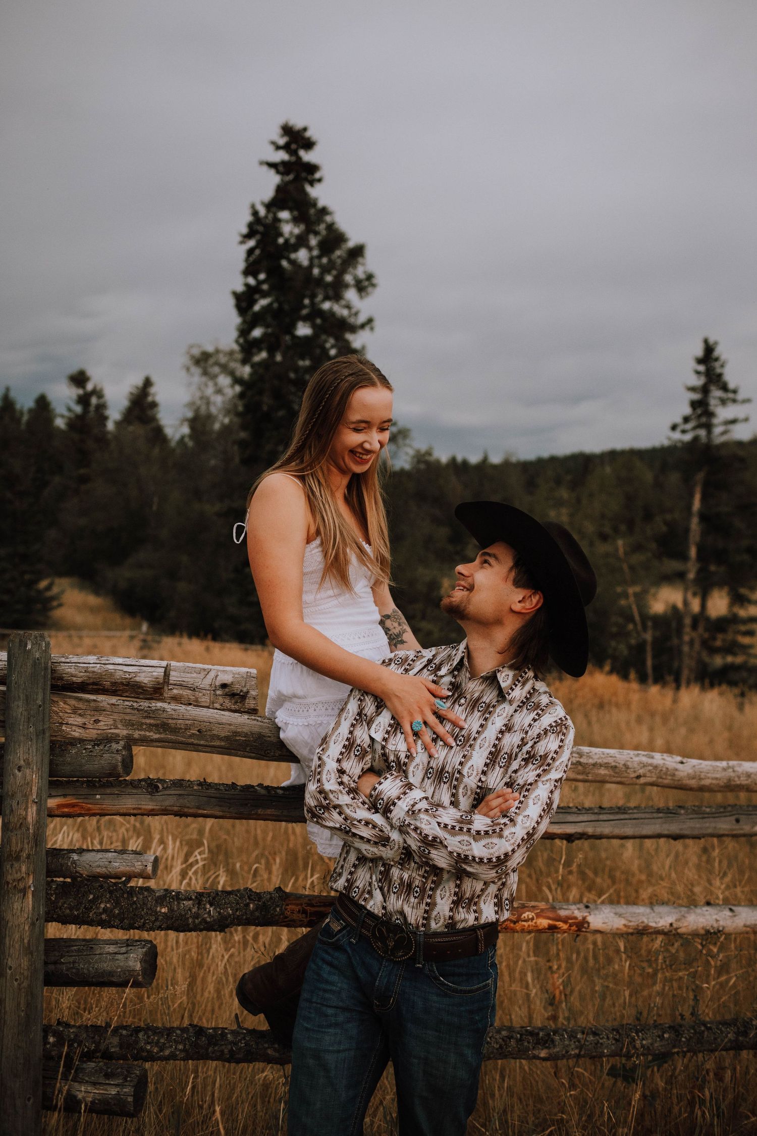 A sweet moment shared between a couple at a rustic wooden fence with mountains in the background.