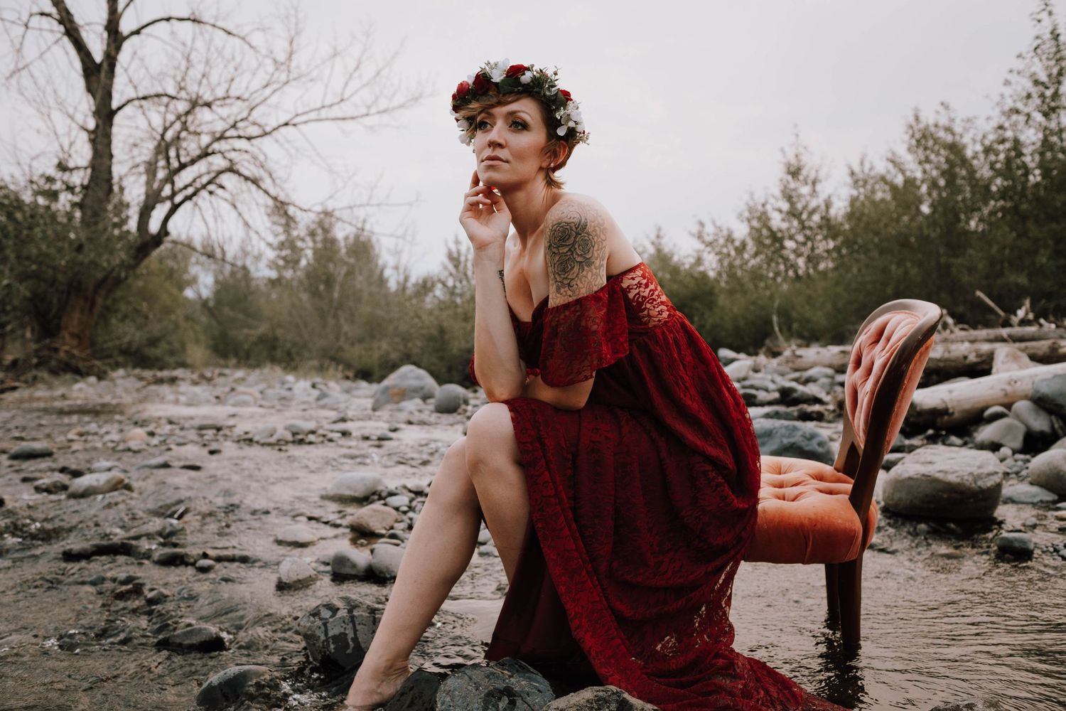Artistic portrait featuring a flowing red dress with a vintage chair on rocky terrain.