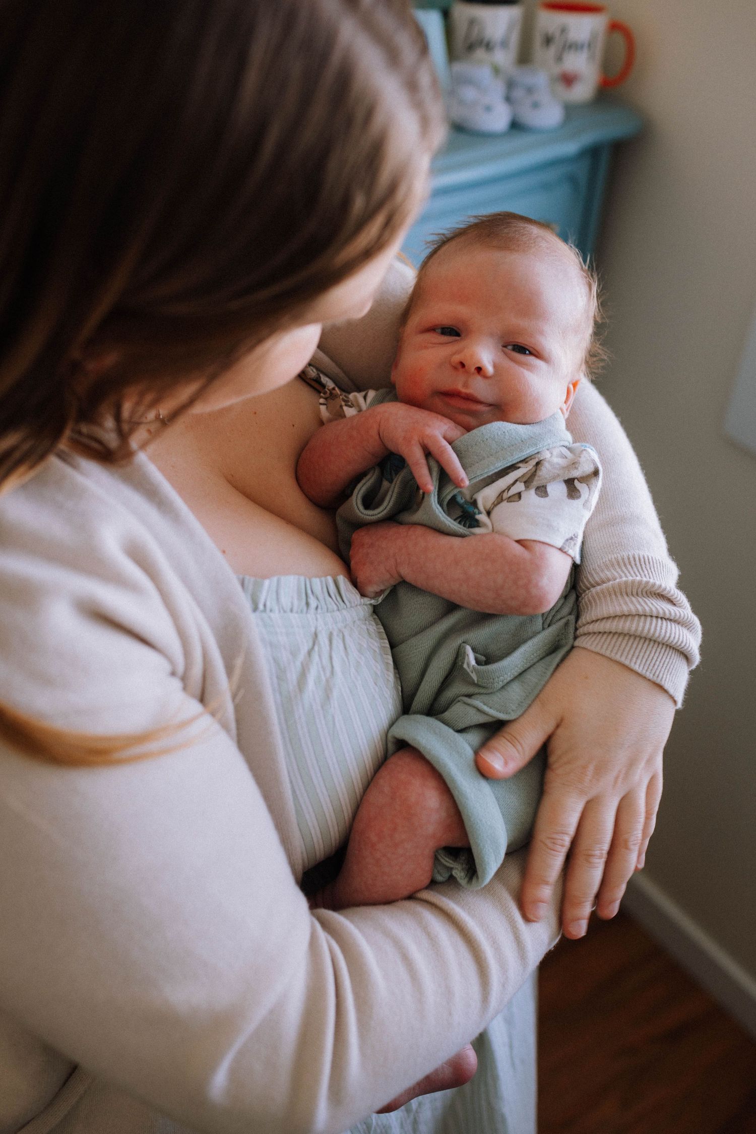 A tender moment as a nurturing caregiver in a cream sweater holds a tiny infant wearing a soft mint green outfit.