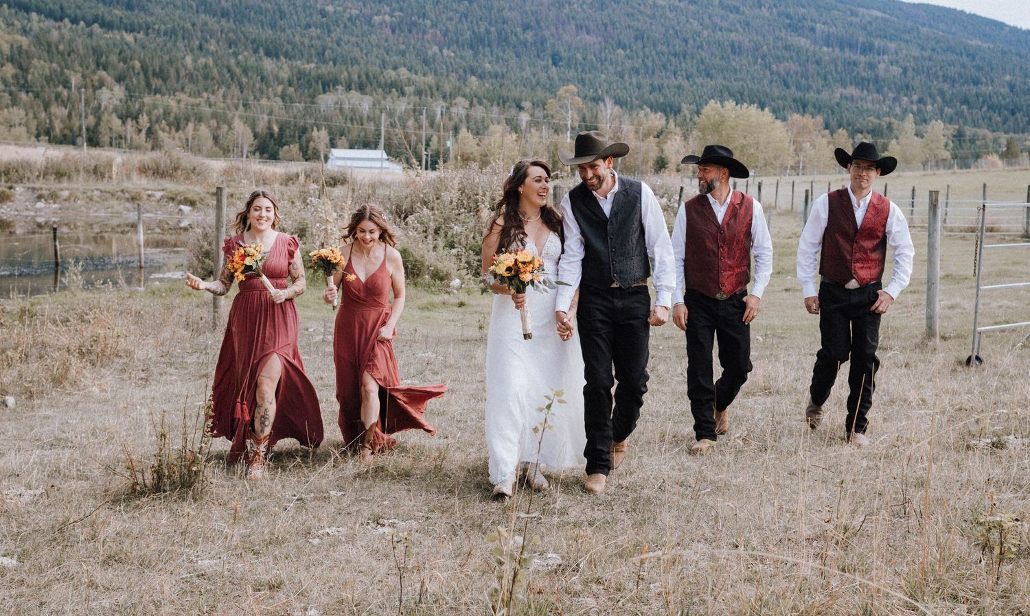 Wedding party poses in rustic western attire against mountain landscape.