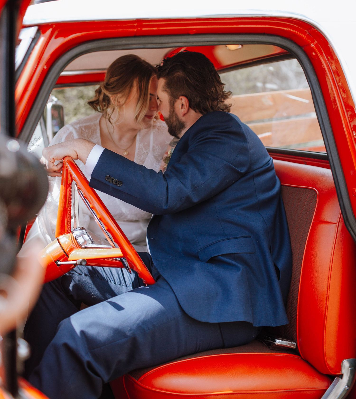 A romantic moment captured inside a classic red car between newlyweds.