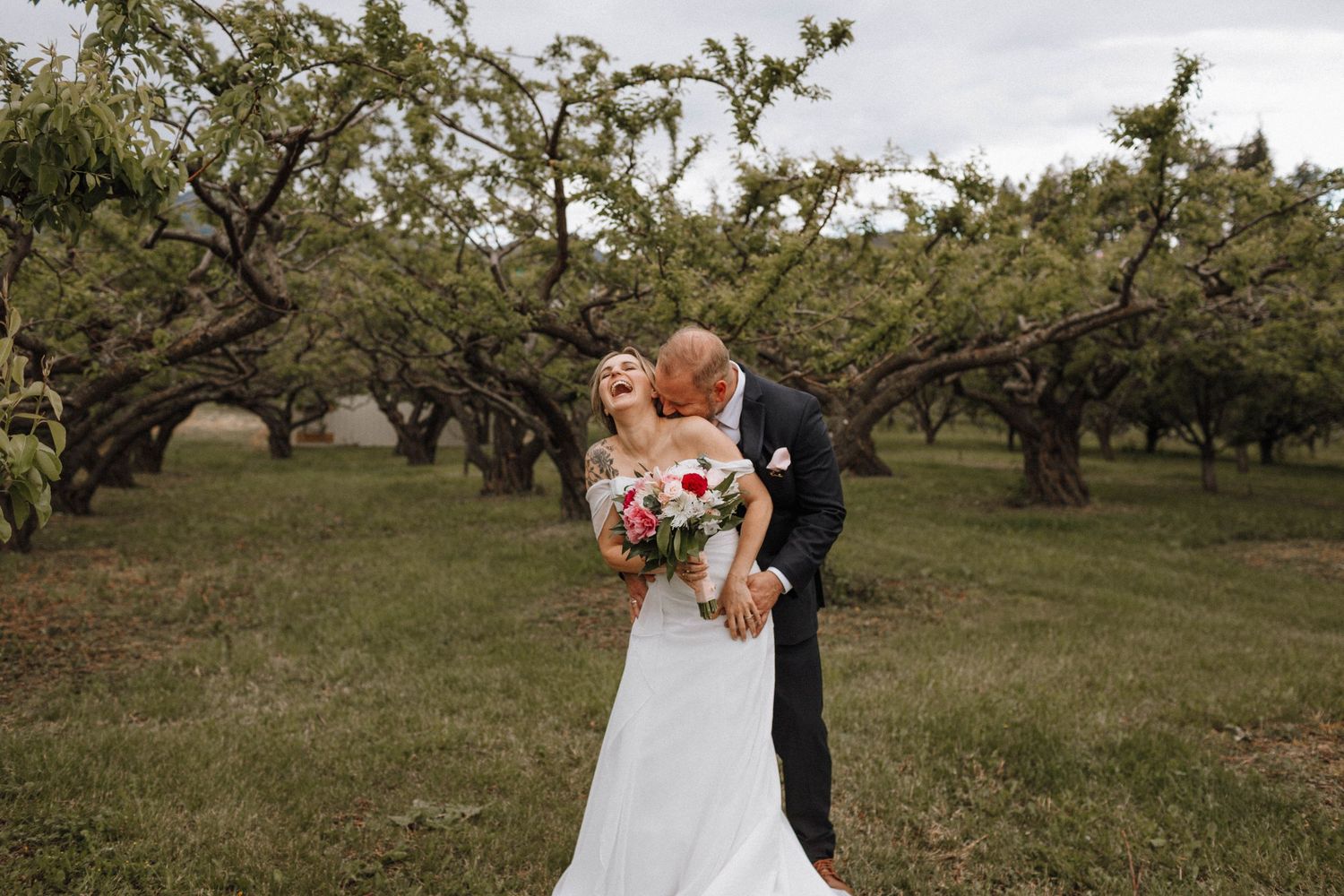 Scenic orchard wedding photo with rustic twisted trees in background.