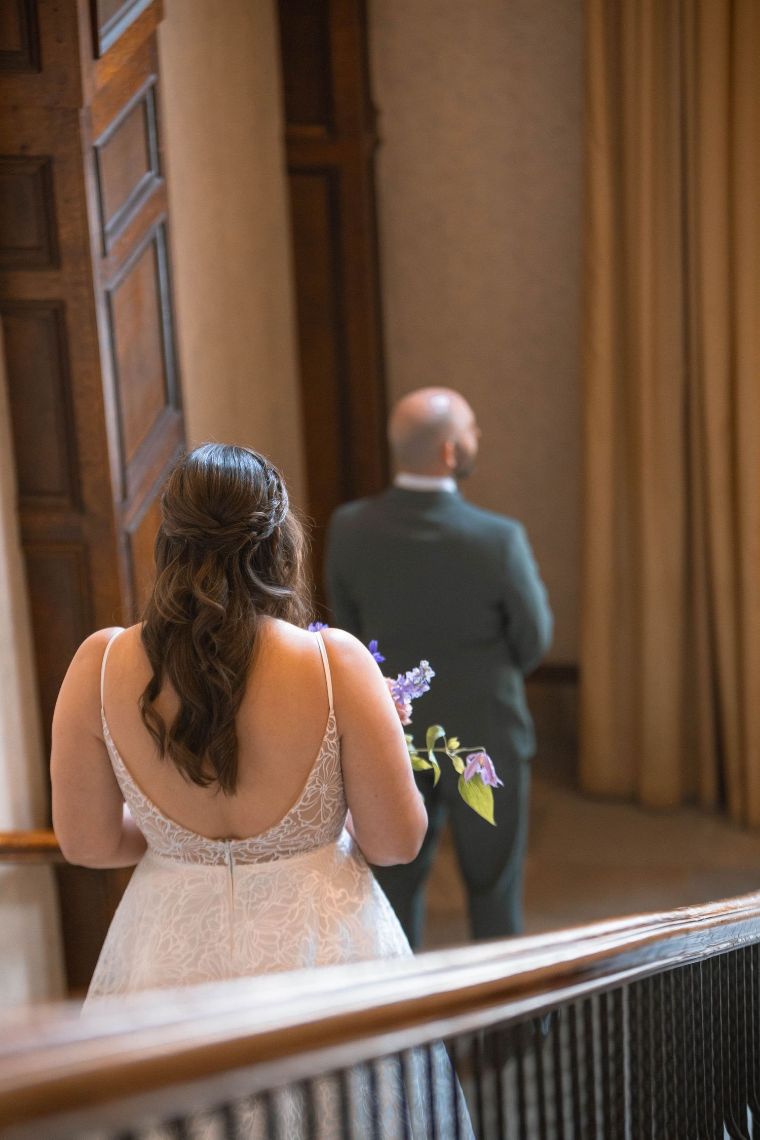Back view of a bride in a lace dress with loose curls standing apart from groom in a dark suit at Sun peaks Grand hotel