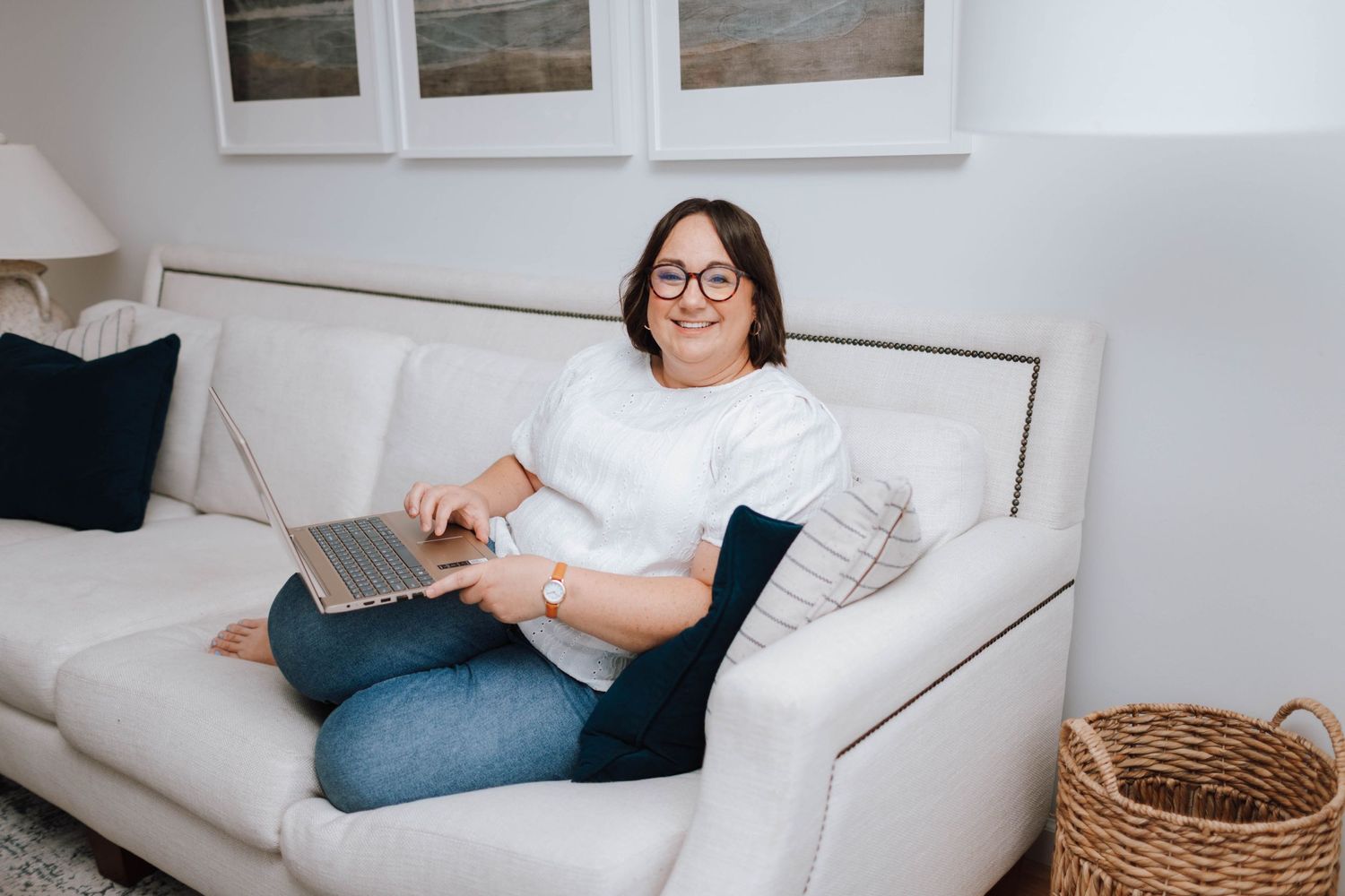 A cozy living room scene with someone relaxing on a white couch with a laptop and throw pillows.