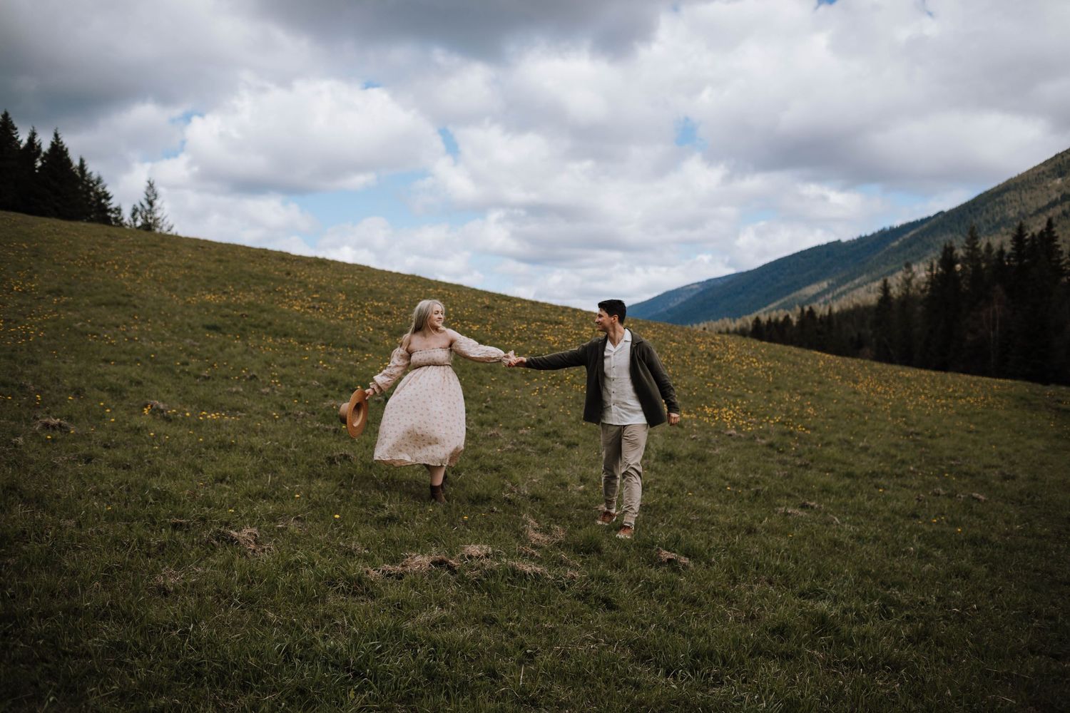 A couple runs hand-in-hand through a mountain meadow wearing wedding attire.