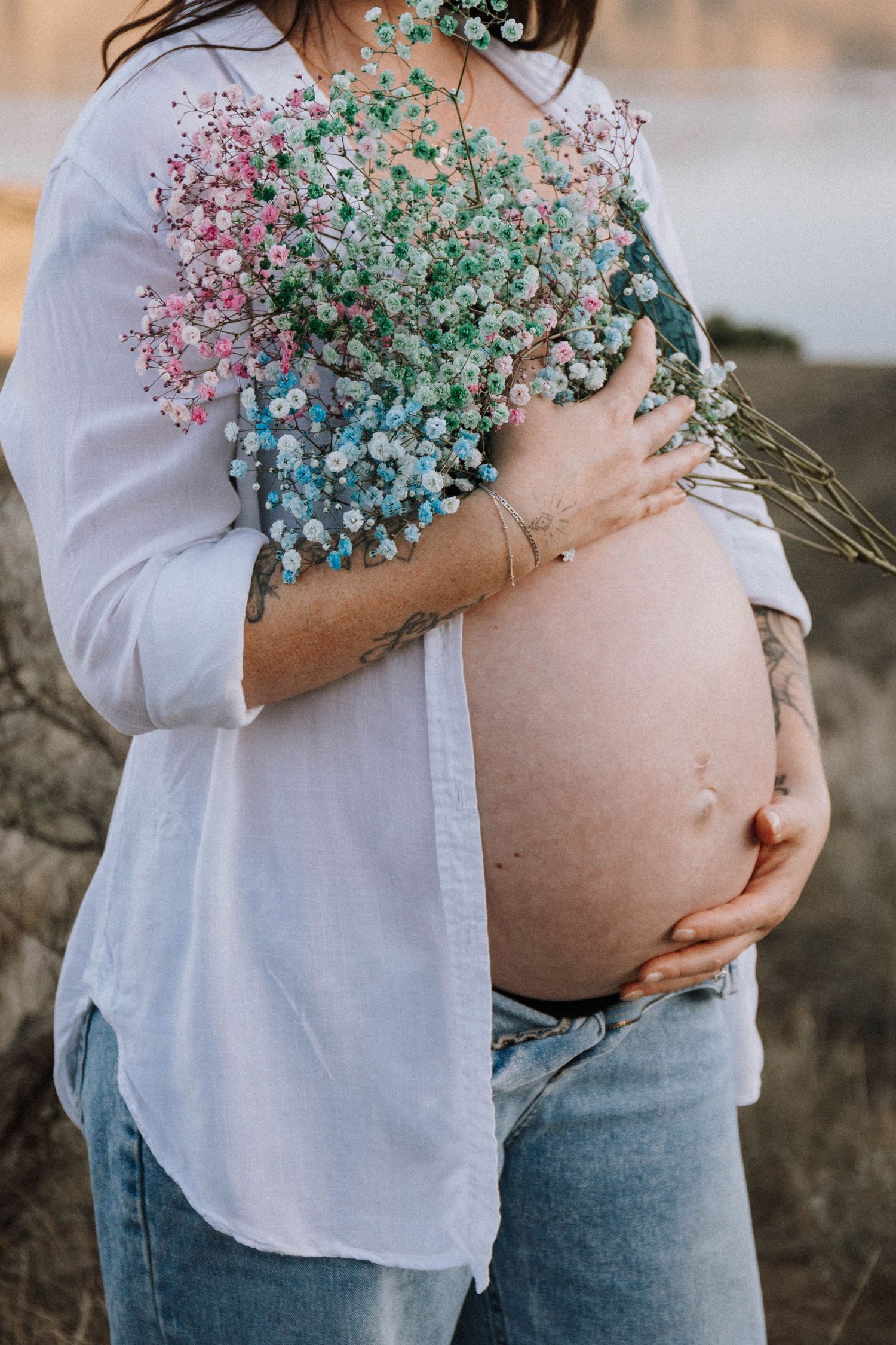 A pregnant belly is tenderly cradled while holding a bouquet of soft pink, mint green and blue baby's breath flowers.