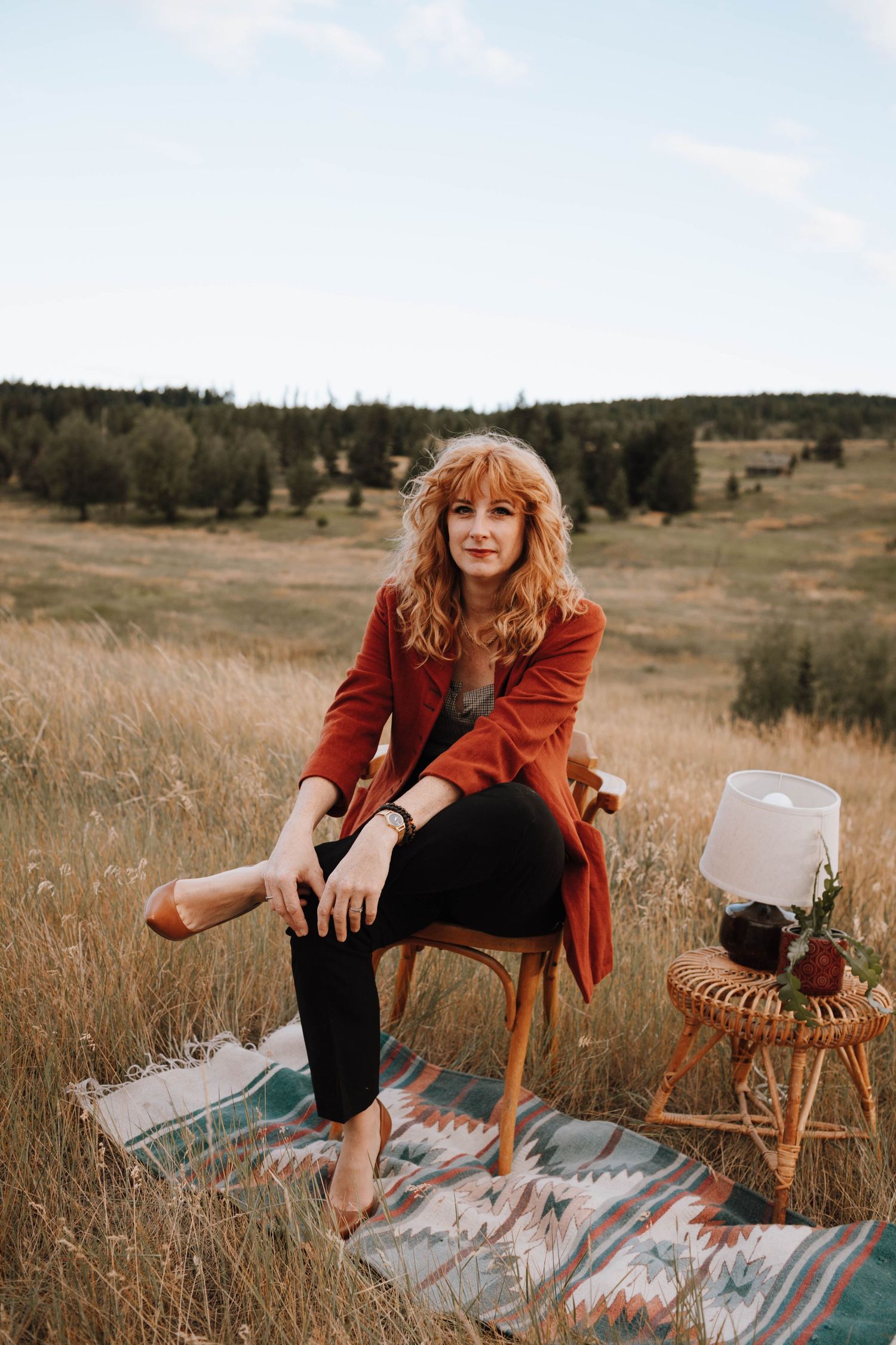Artistic outdoor portrait with wooden chair and vintage styling against mountain backdrop.