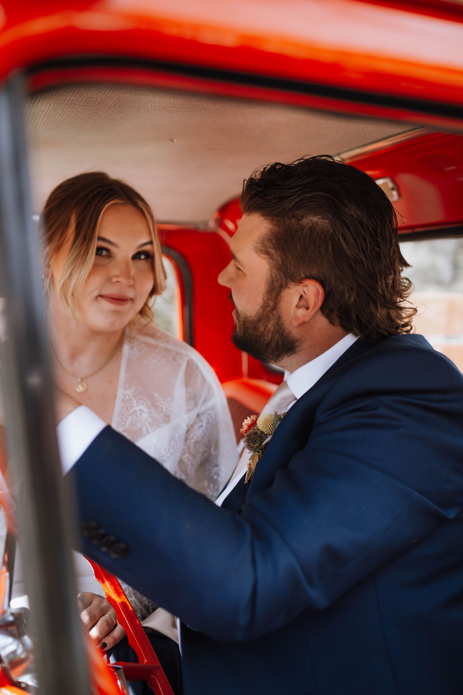 A wedding couple shares an intimate moment inside a vintage red vehicle.