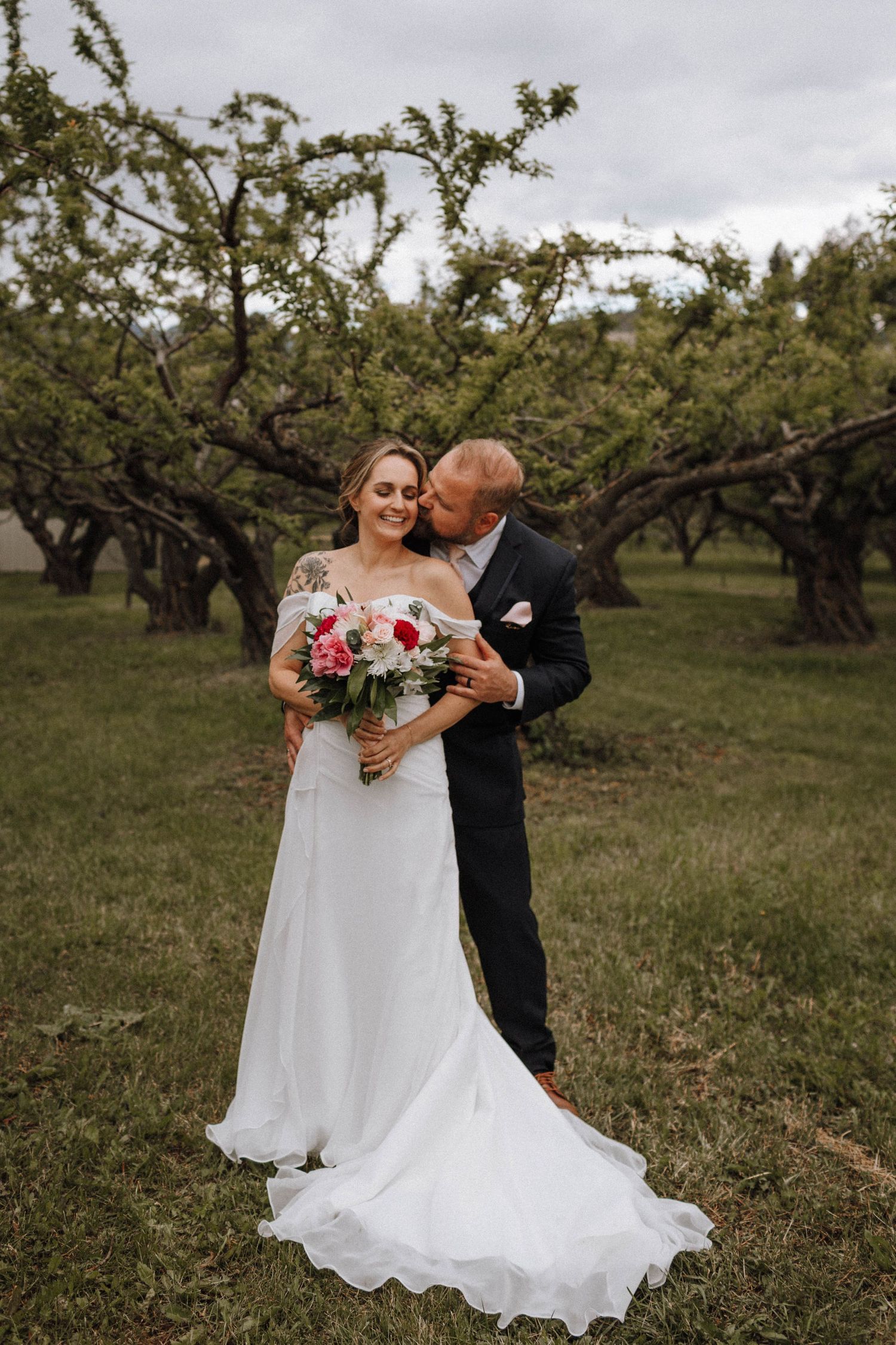 Elegant wedding portrait in apple orchard with flowing white dress and bouquet.