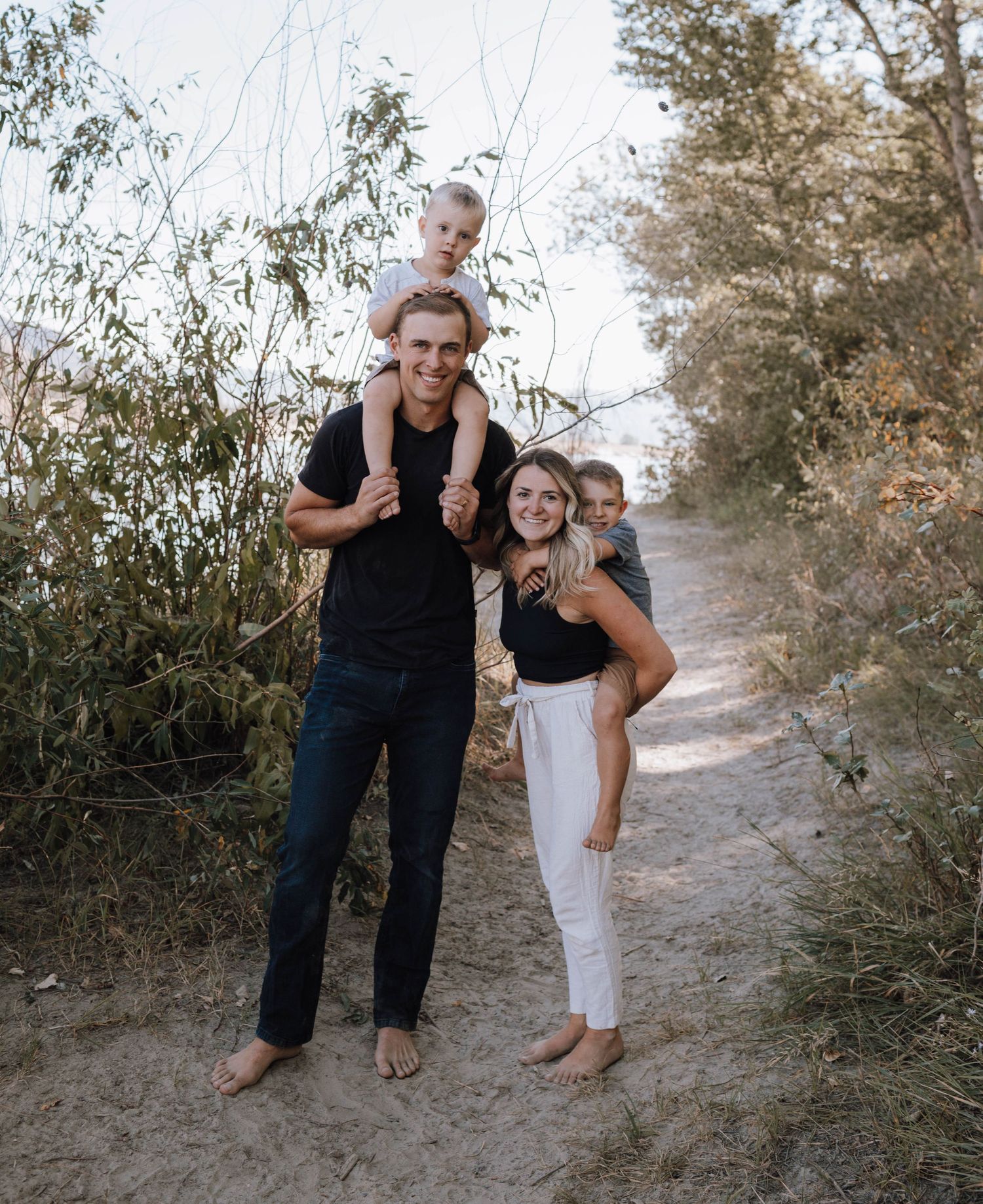 A family in matching black shirts poses together on a dirt path surrounded by greenery on a sunny day.