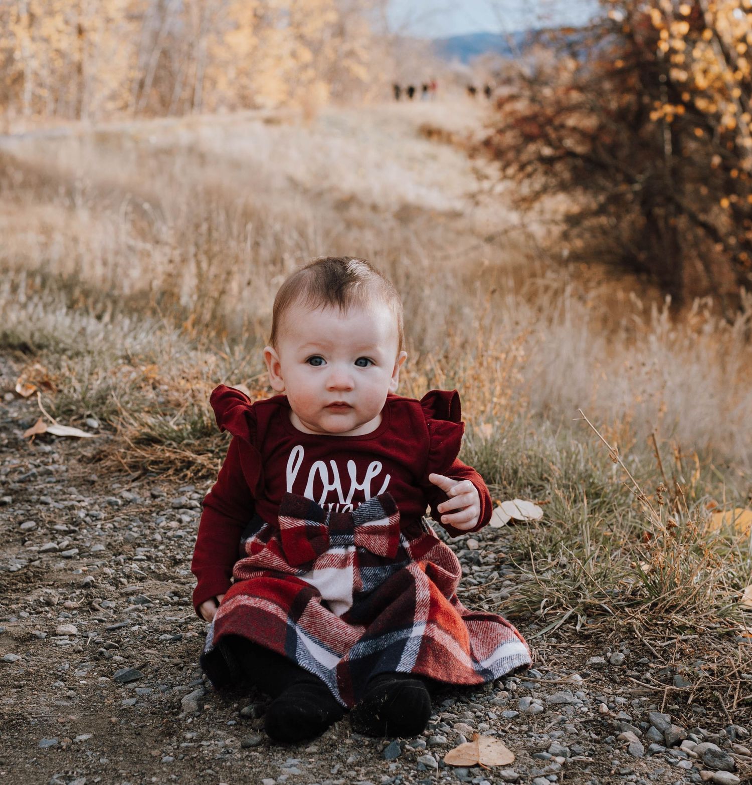 Child in red sweater sitting on autumn trail.