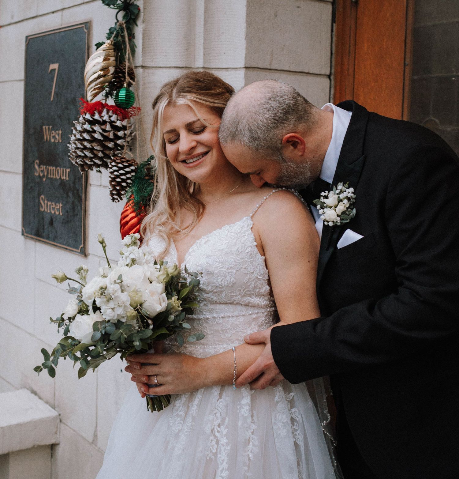Intimate moment at historic building entrance with white floral bouquet and holiday decor.