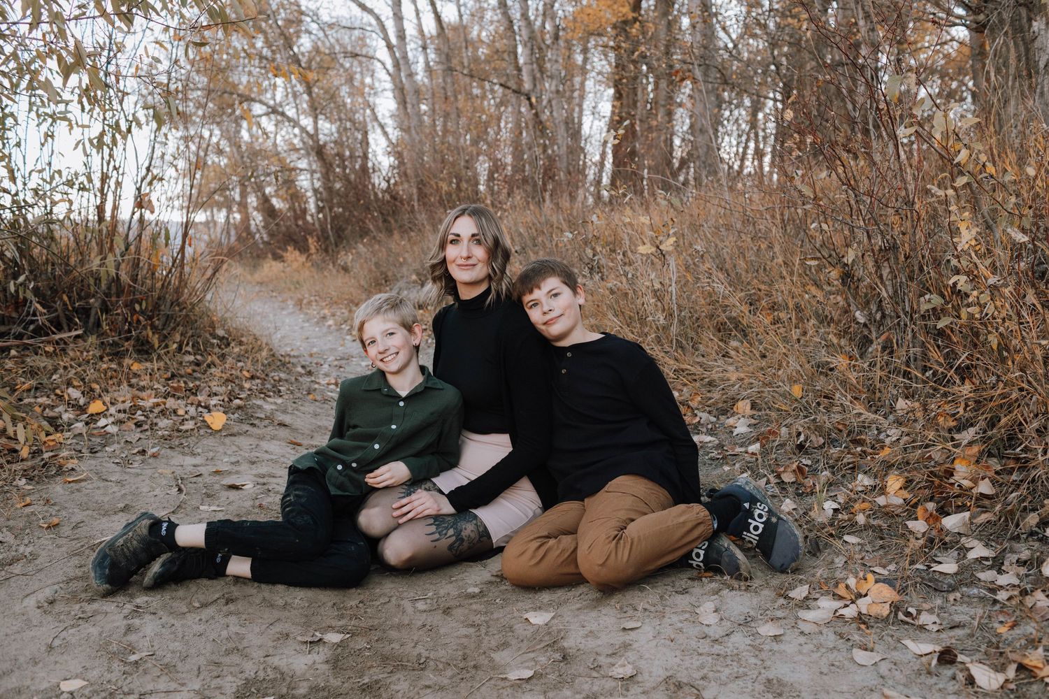A family sits together on a dirt path surrounded by fall foliage.