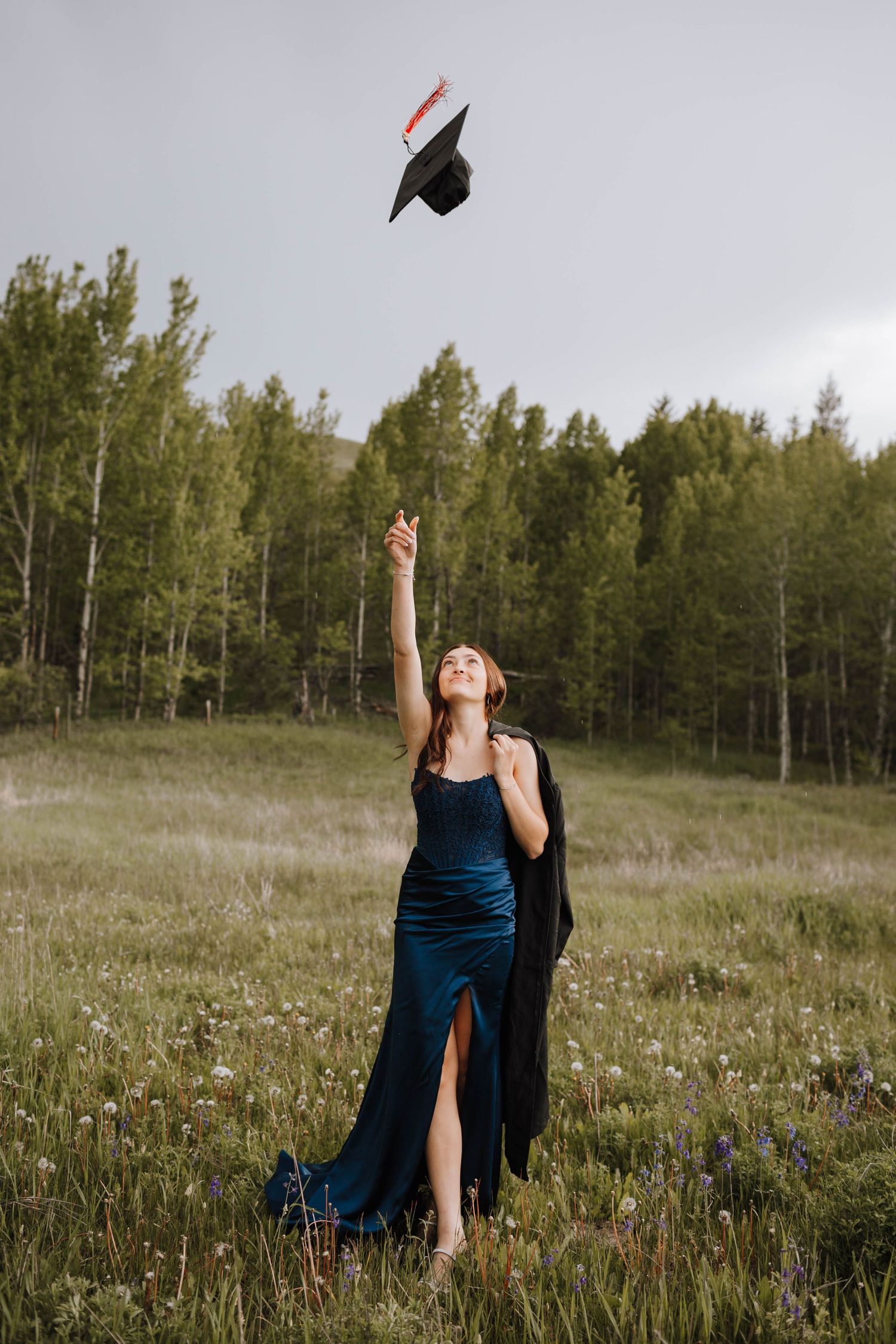 A graduation cap is tossed in the air against a backdrop of aspen trees and mountain meadow.