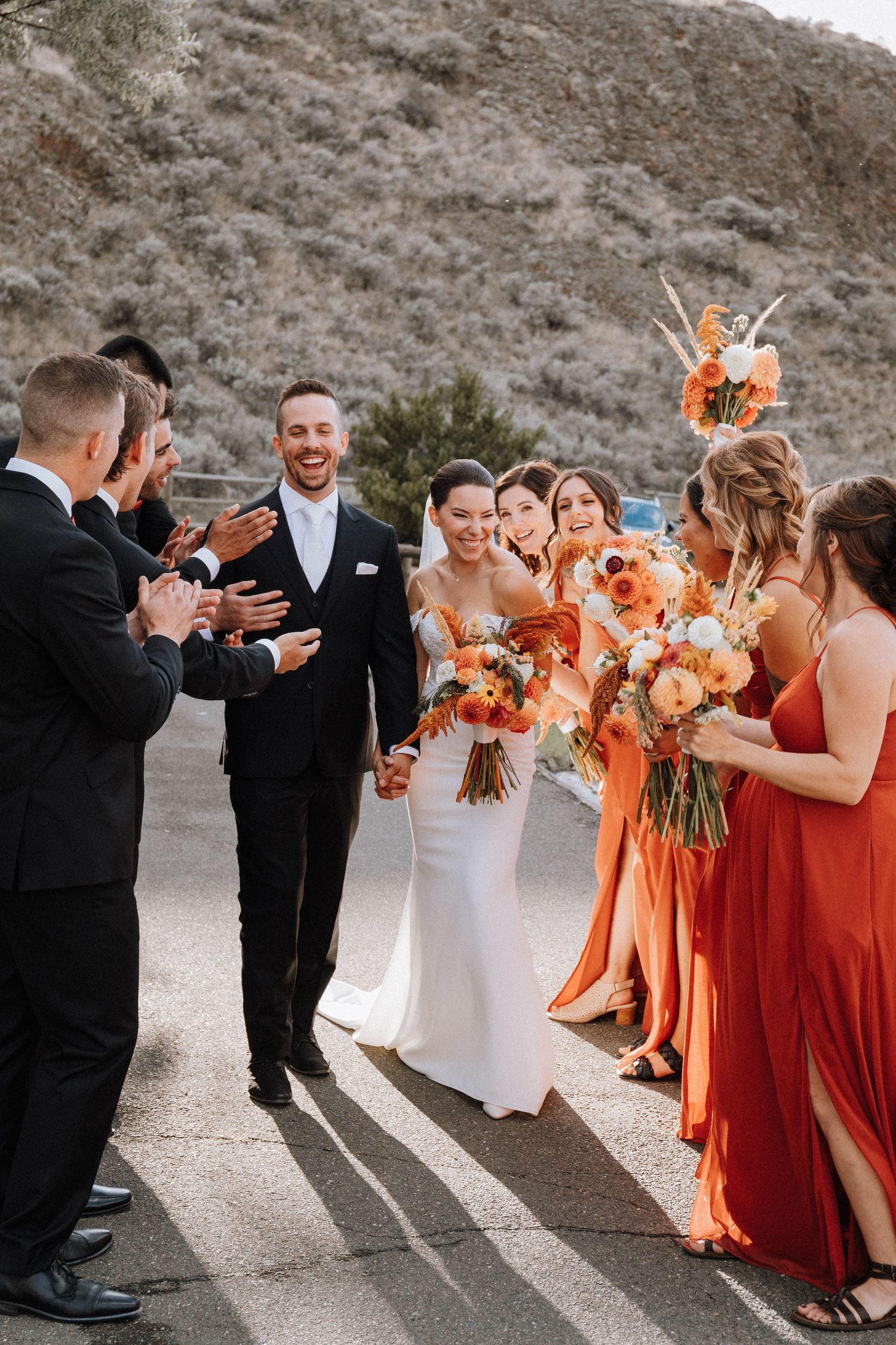 Celebration moment with wedding party wearing orange dresses and black suits on outdoor path.
