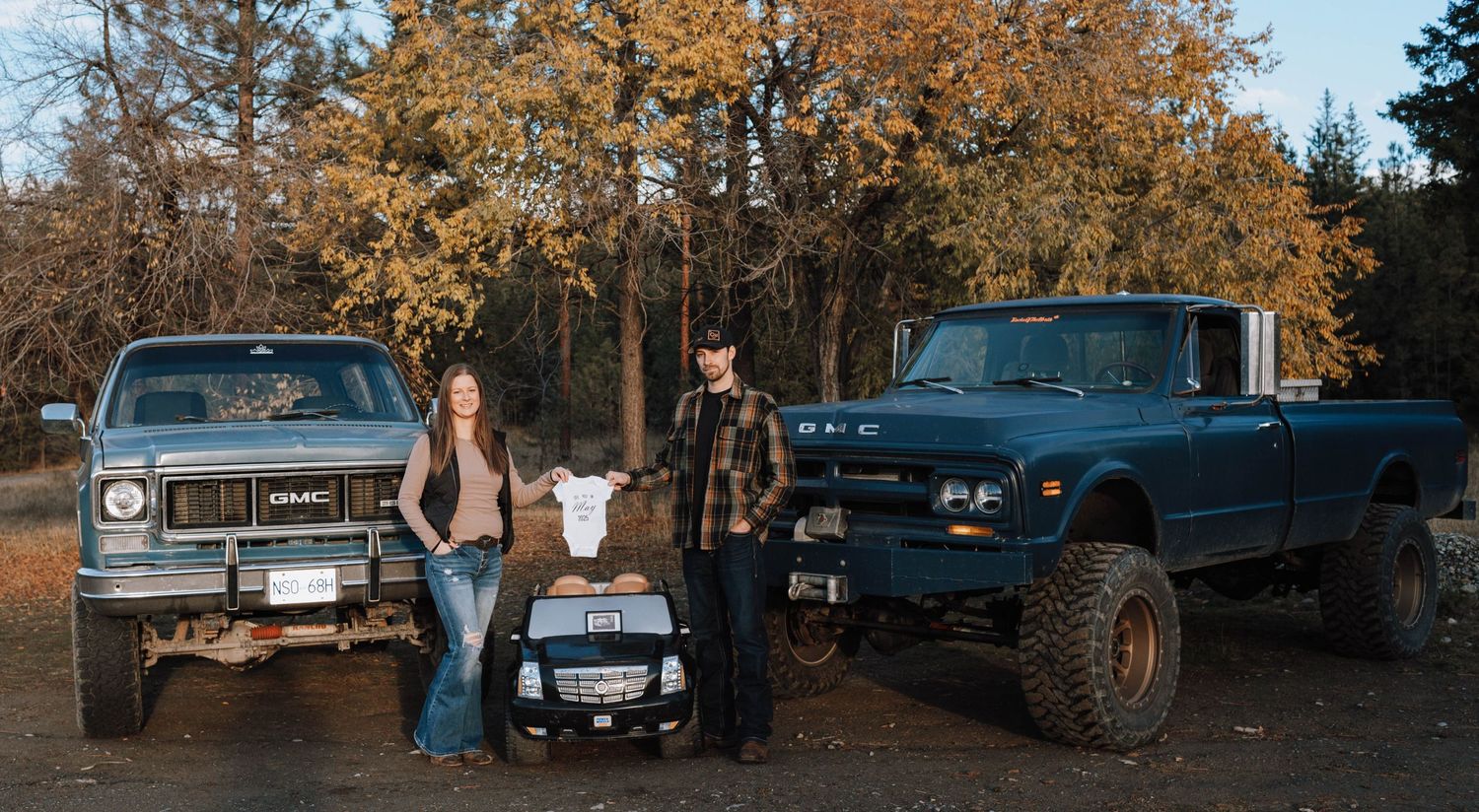 A family stands between two rugged trucks with a small toy Cadillac Escalade in an autumn setting.