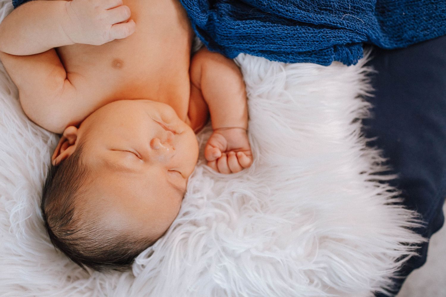 Peaceful sleeping baby on white fur rug with blue fabric.