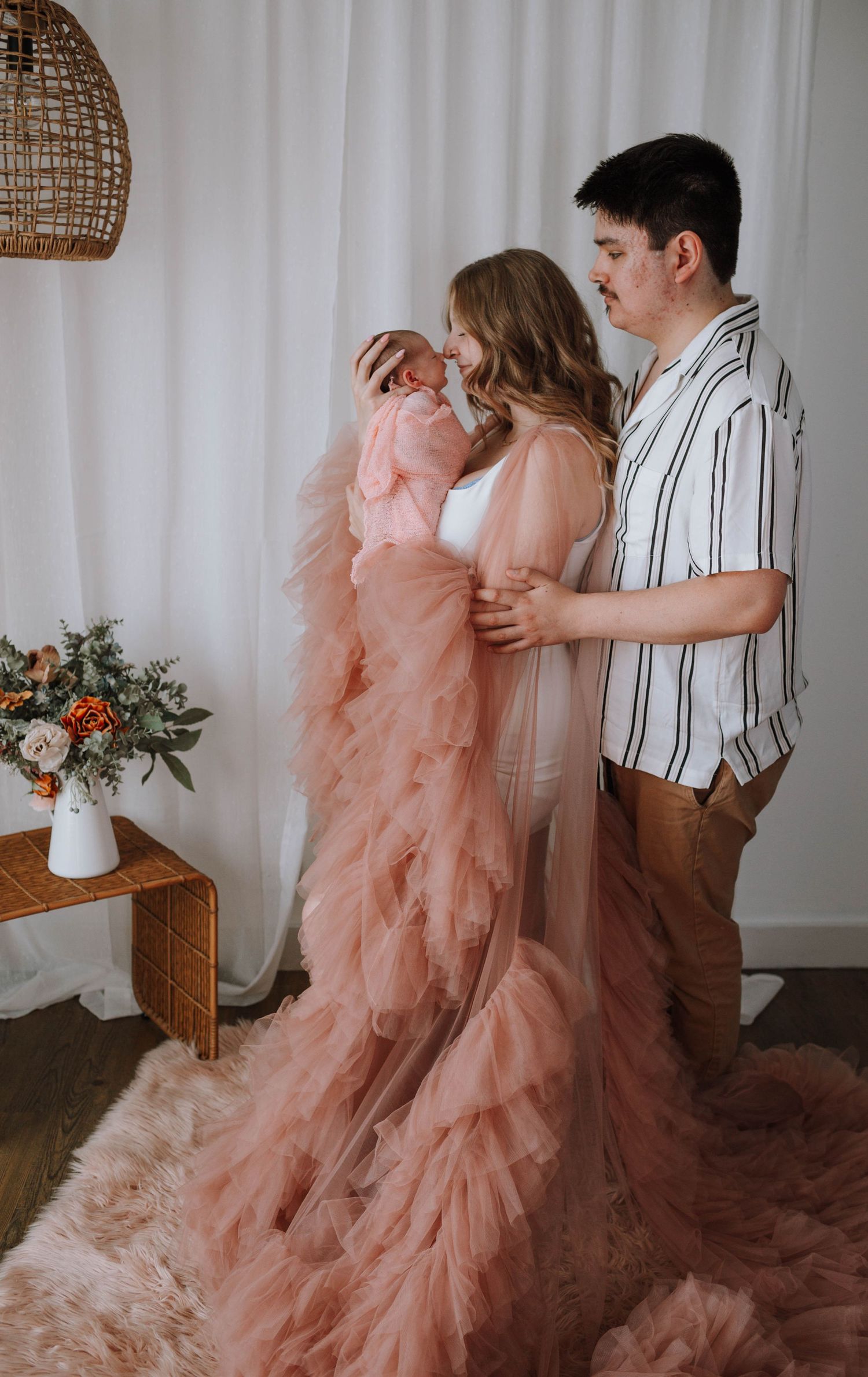 Couple in elegant attire embracing with flowing pink dress in modern room setting.