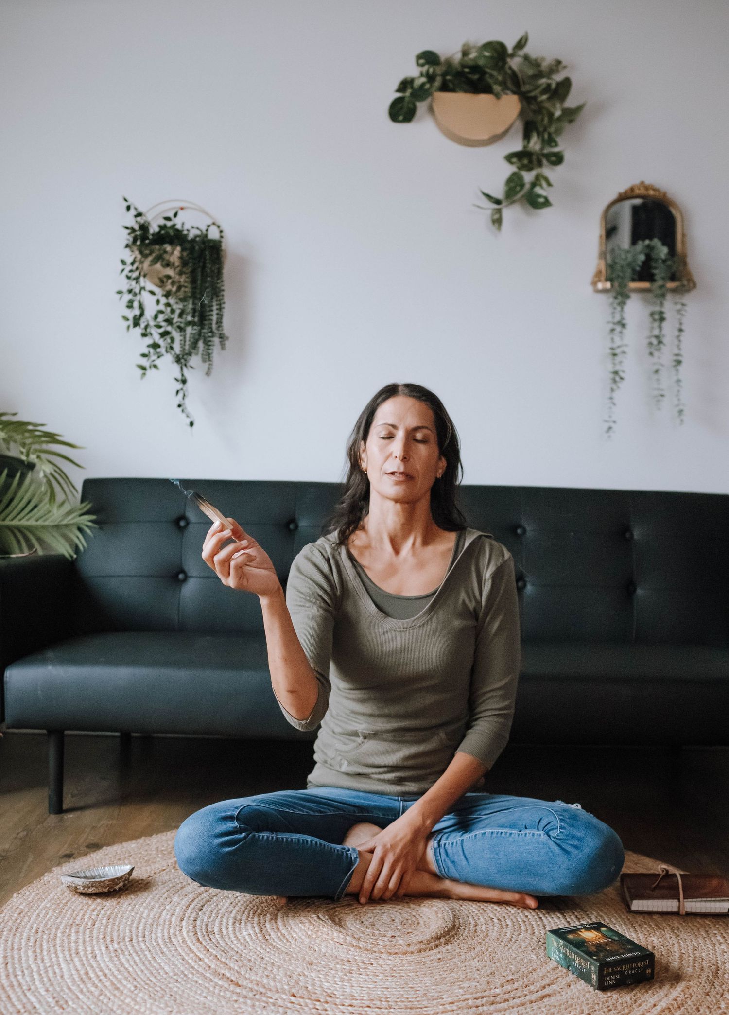 A contemplative indoor scene with hanging plants, a dark sofa, and a person sitting on a round rug.