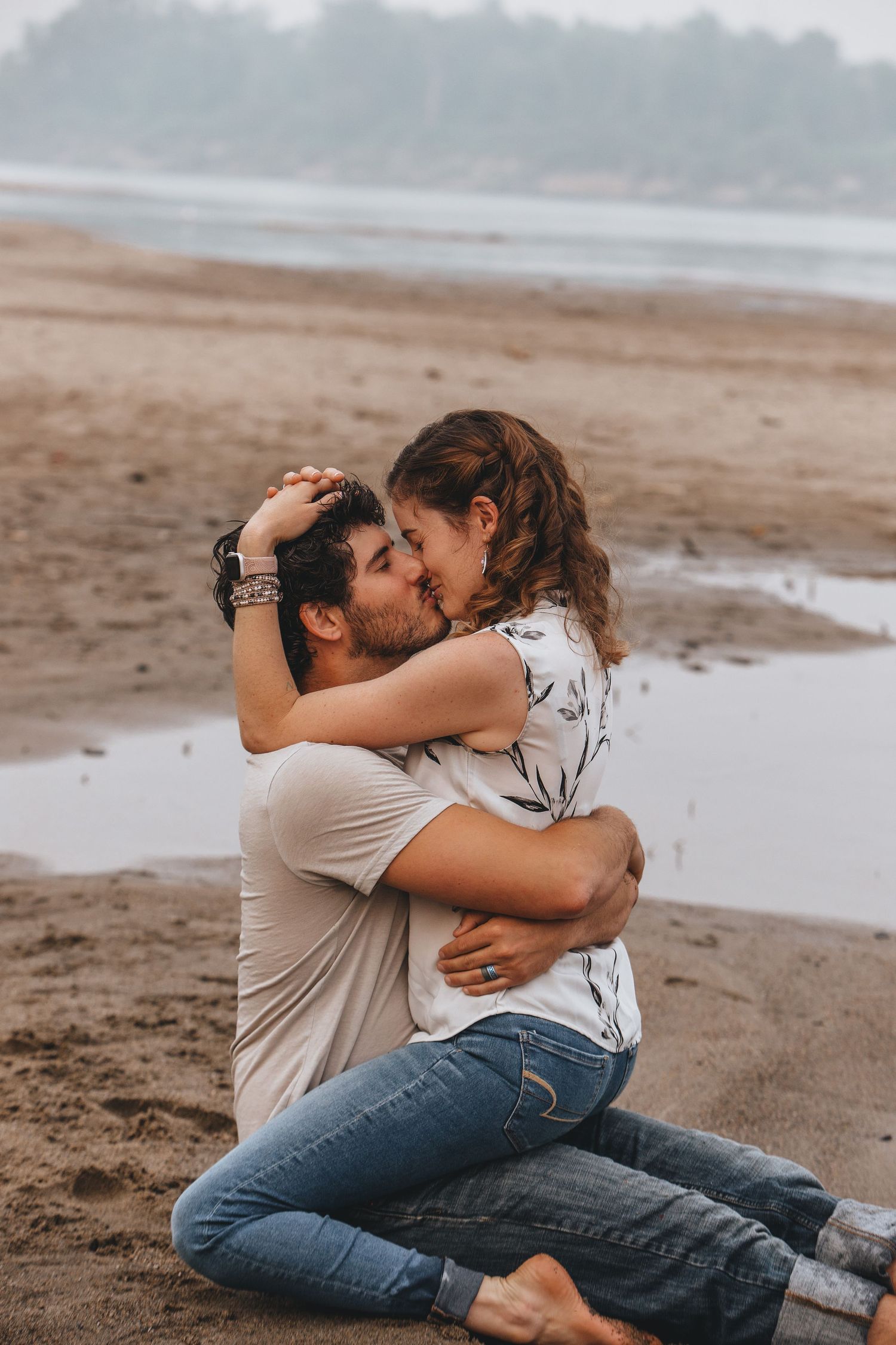 A couple shares intimate moments on a misty beach while sitting in the sand.