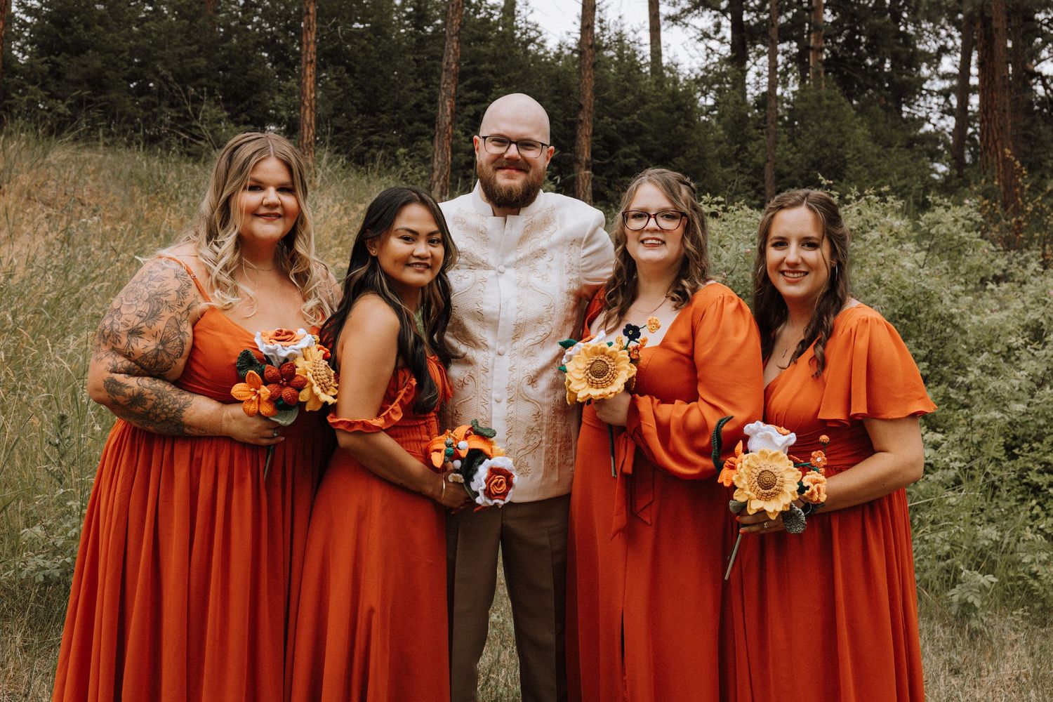 A group in coordinating orange and white outfits poses together for outdoor autumn photos in a wooded setting.