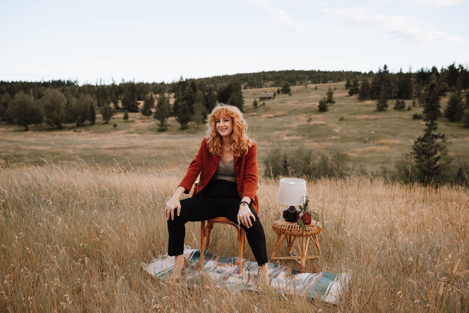 Person in red sweater sitting on blanket in mountain meadow with tarot cards.