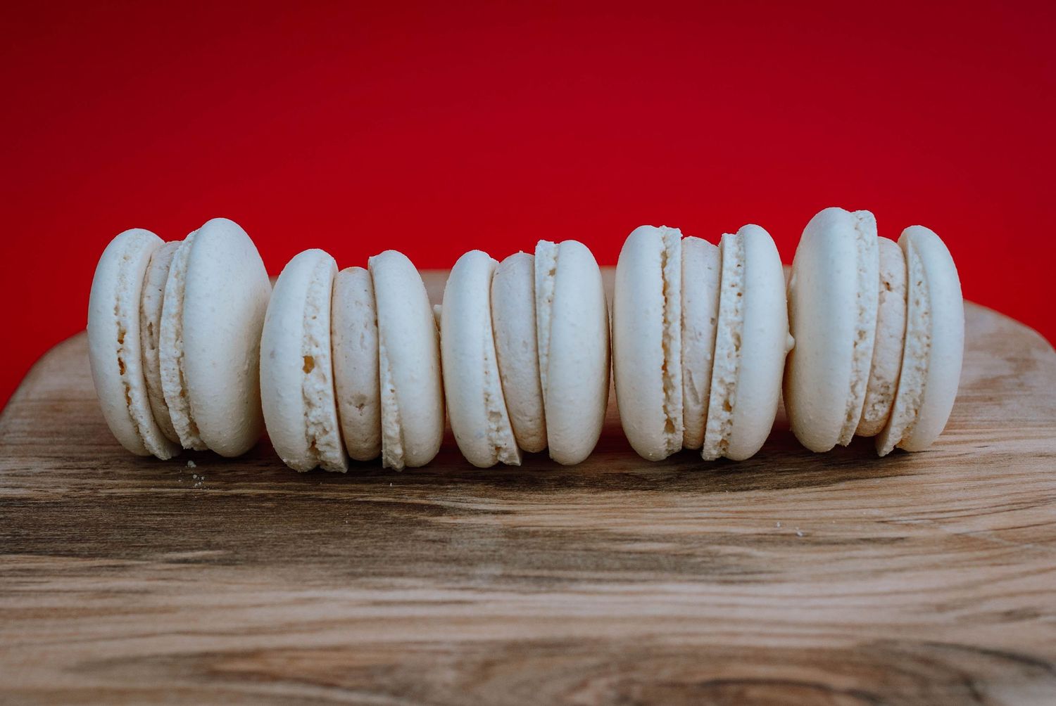 Row of white macarons arranged on wooden surface against vibrant red background.