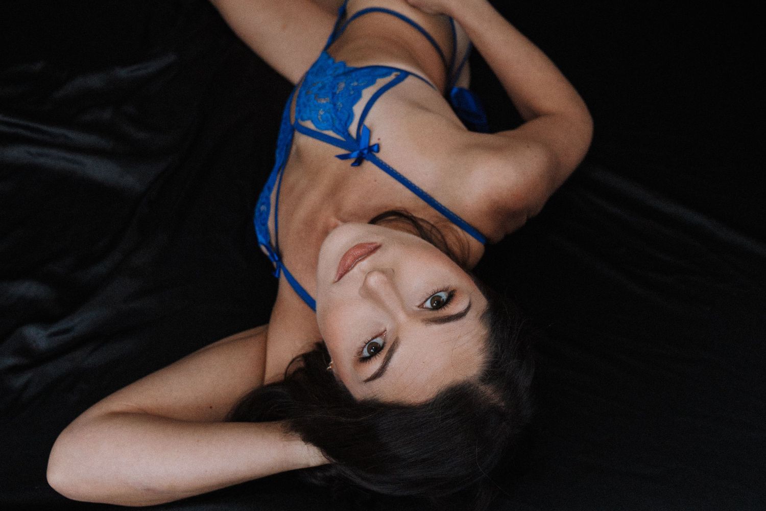 A figure in a black dress and blue ribbon poses gracefully against a dark background in a series of artistic portraits.