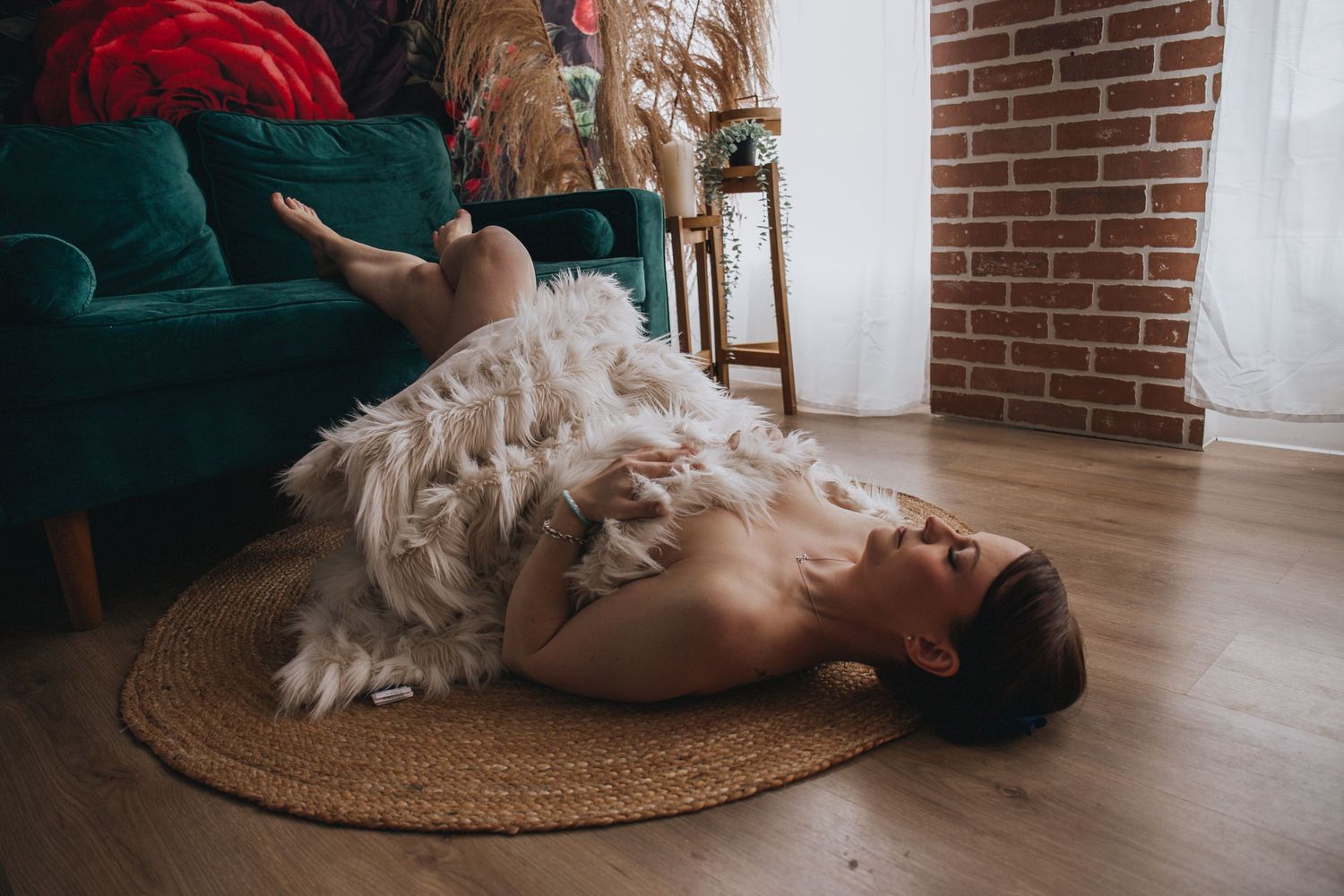 Romantic portrait with white feather boa on hardwood floor near emerald velvet chair.