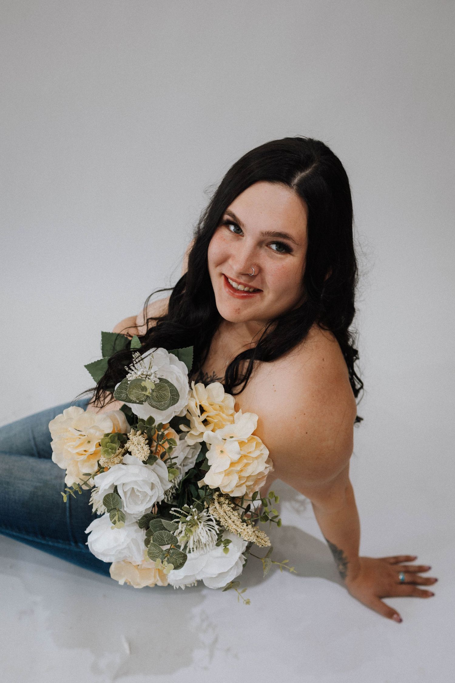 Beautiful bridal boudoir portrait featuring a bouquet with white and cream flowers and greenery on a light background.