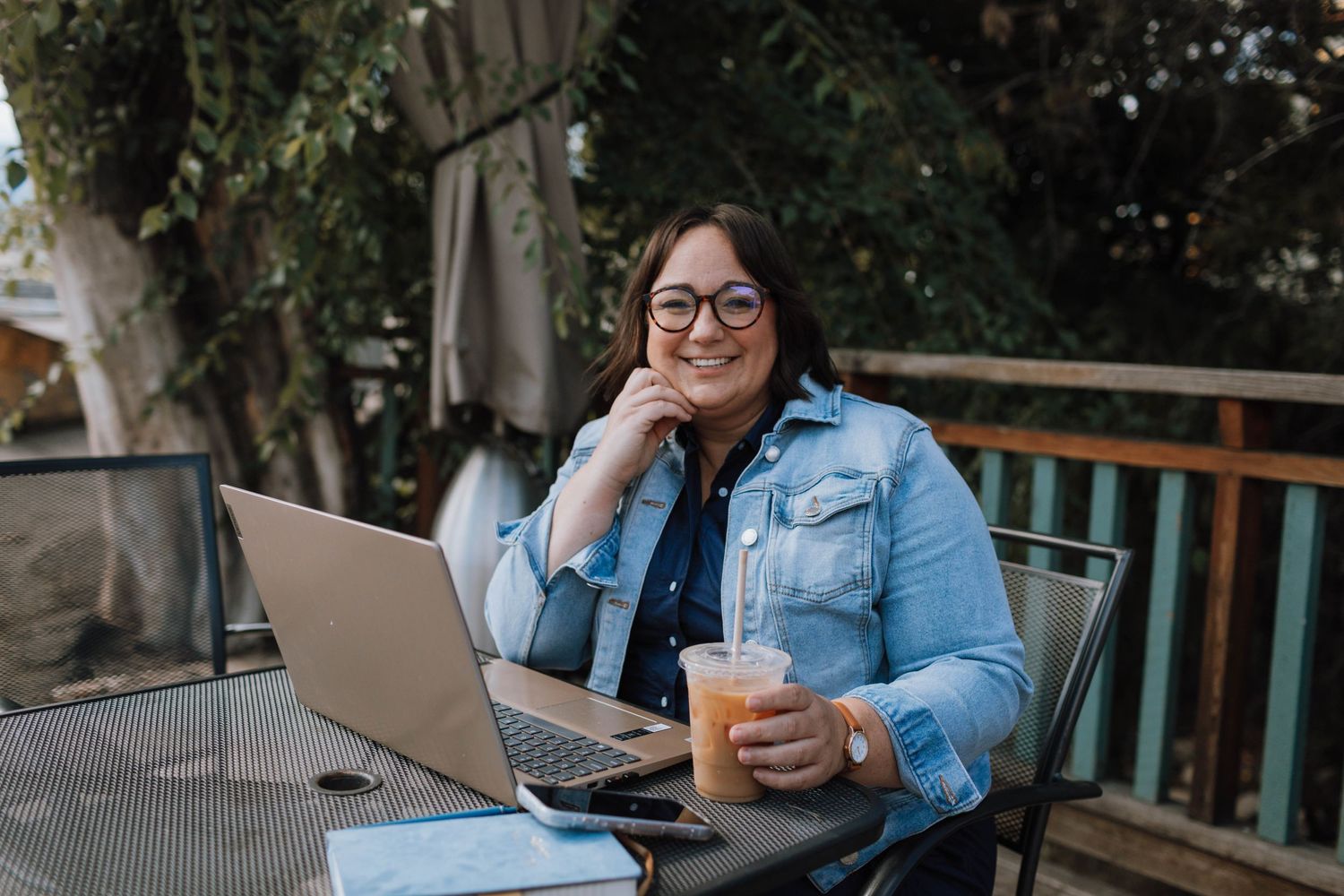 Outdoor cafe workspace with laptop and iced coffee drink on metal table.