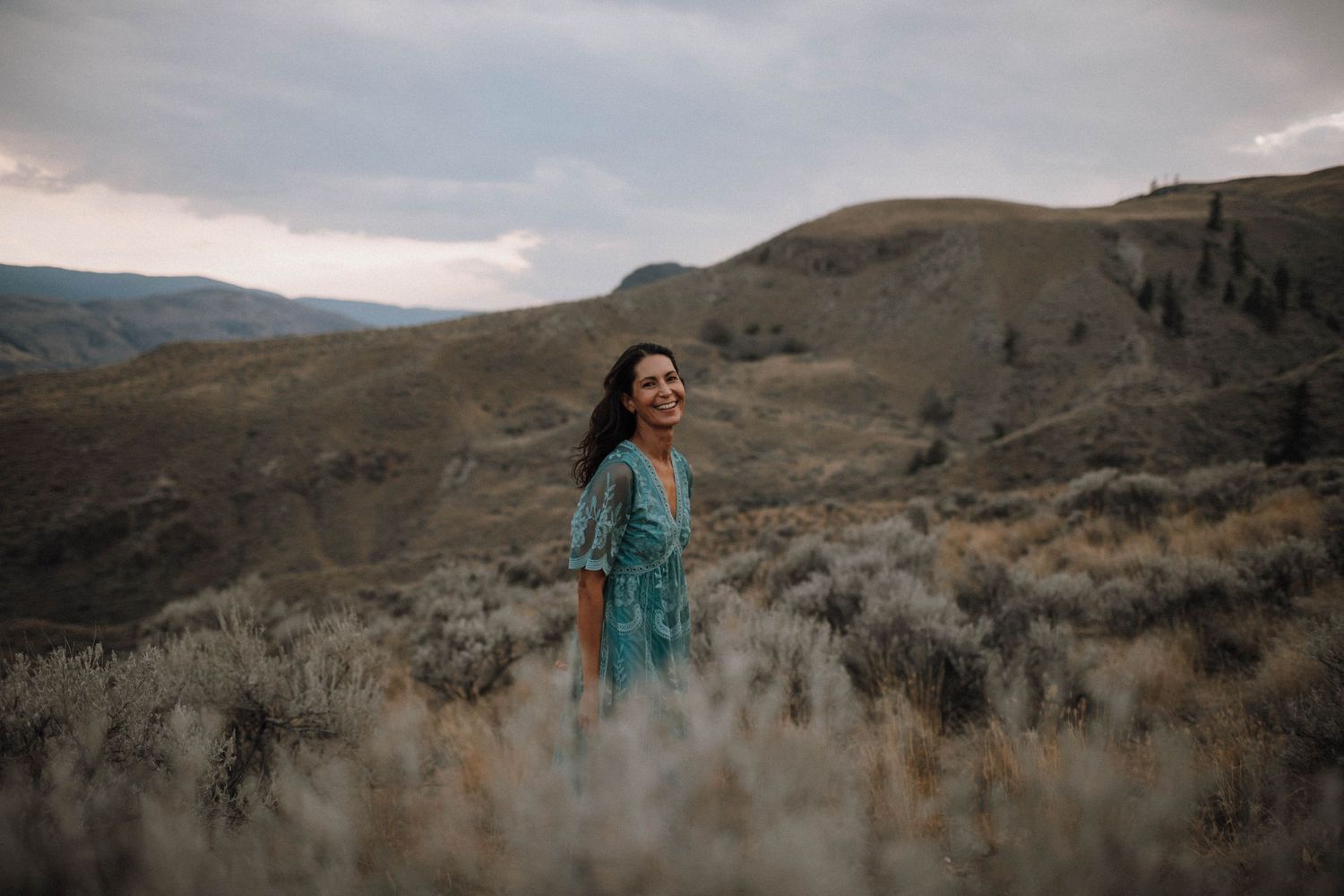 Teal dress flows in the wind against dramatic desert mountain landscape.