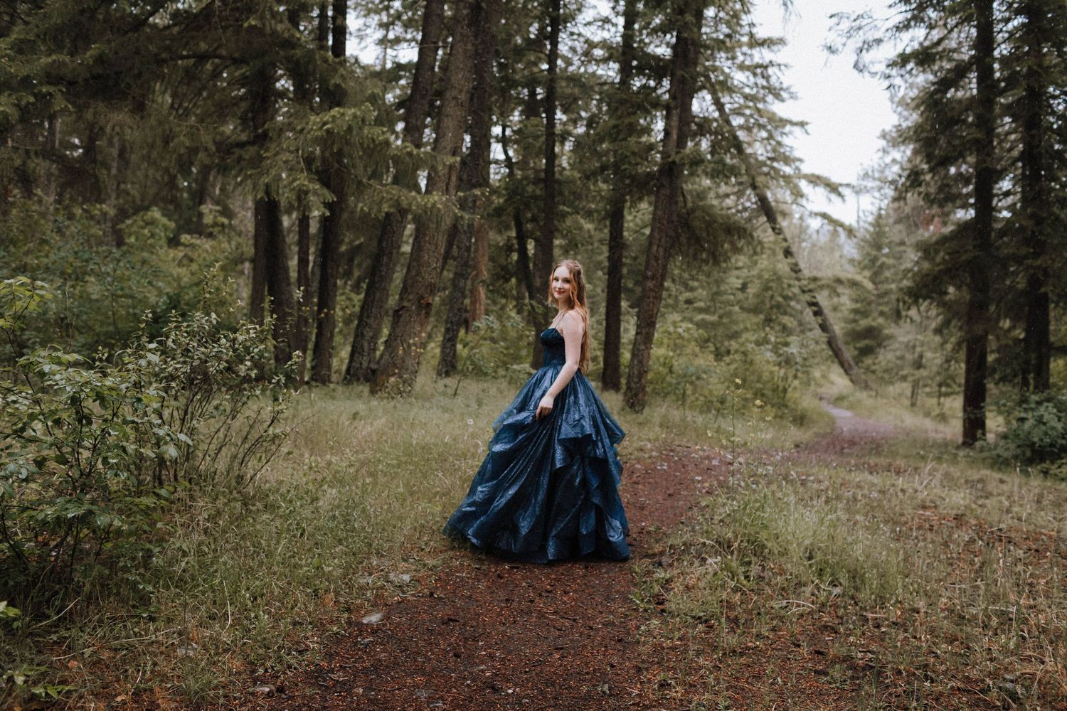 A flowing navy blue gown creates dramatic contrast against the green forest setting.