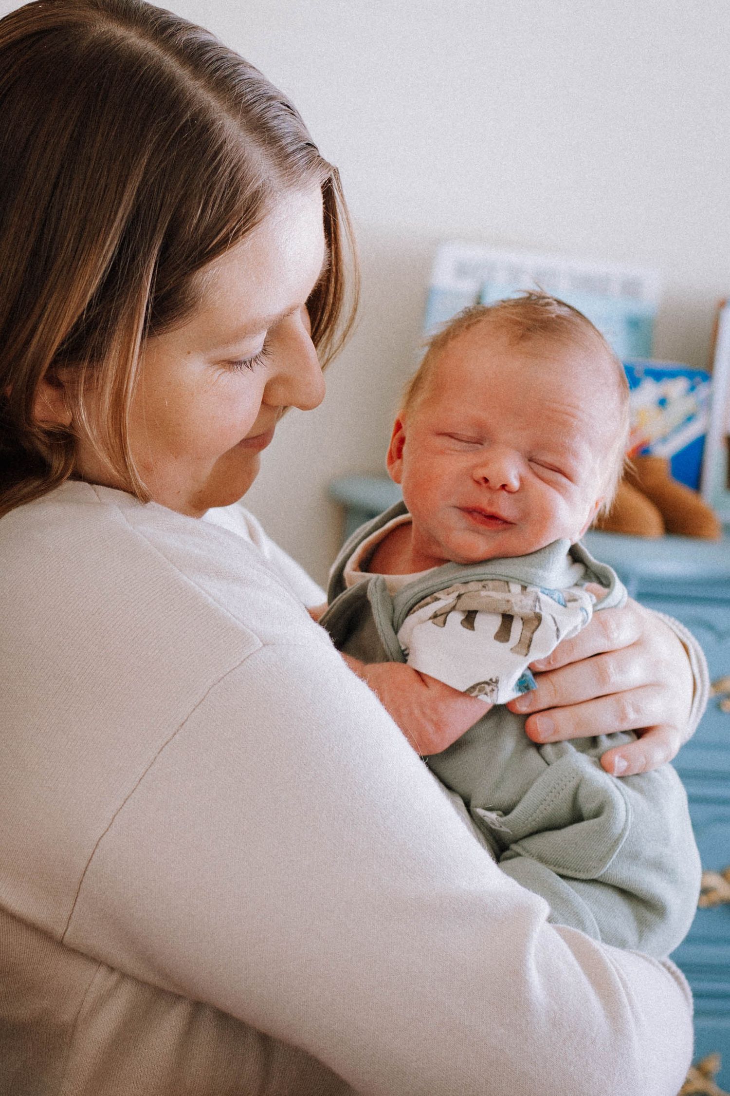 A tender moment between mother and newborn baby in a white sweater against a soft hospital backdrop.
