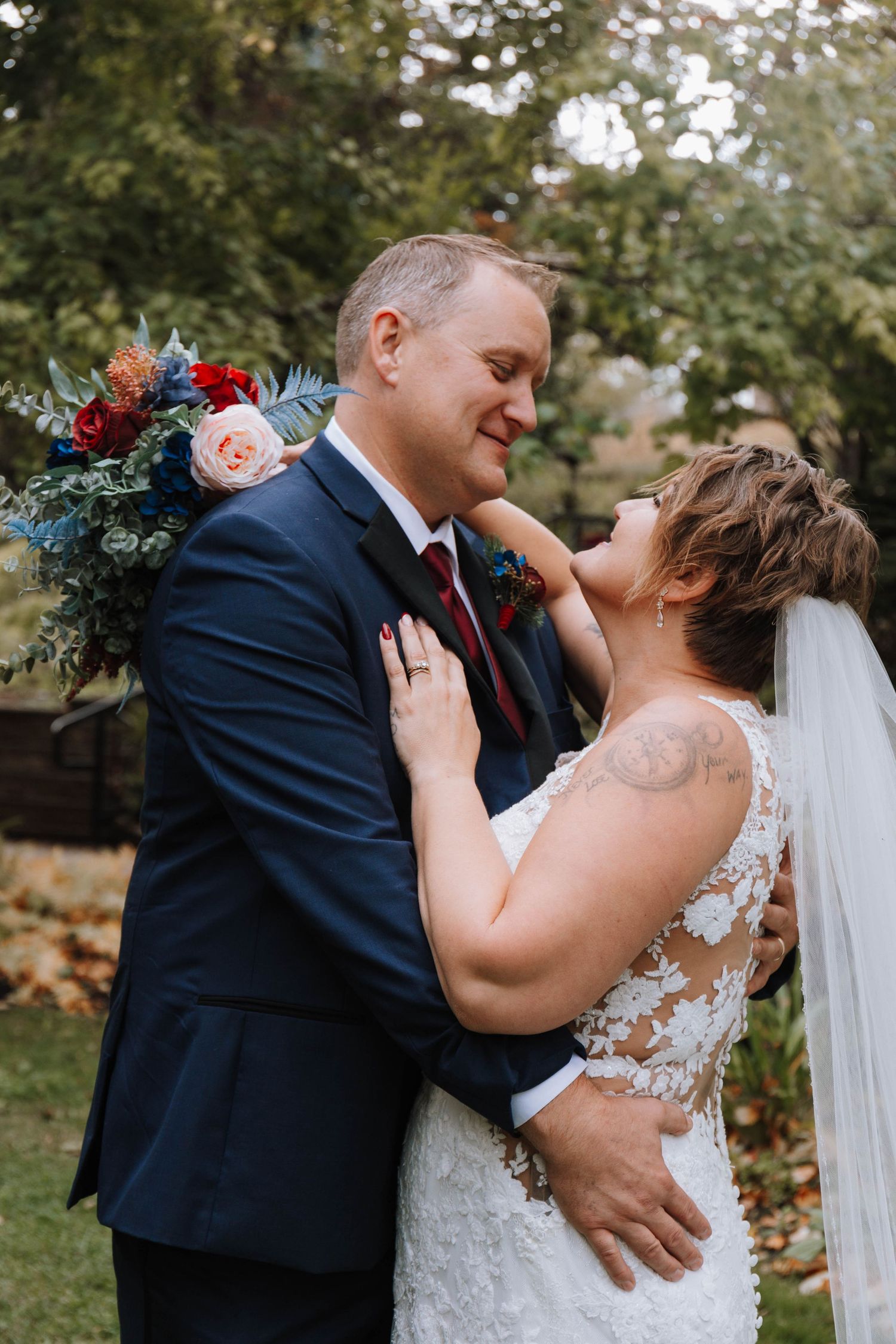 Wedding couple embraces in garden setting with colorful floral bouquet.