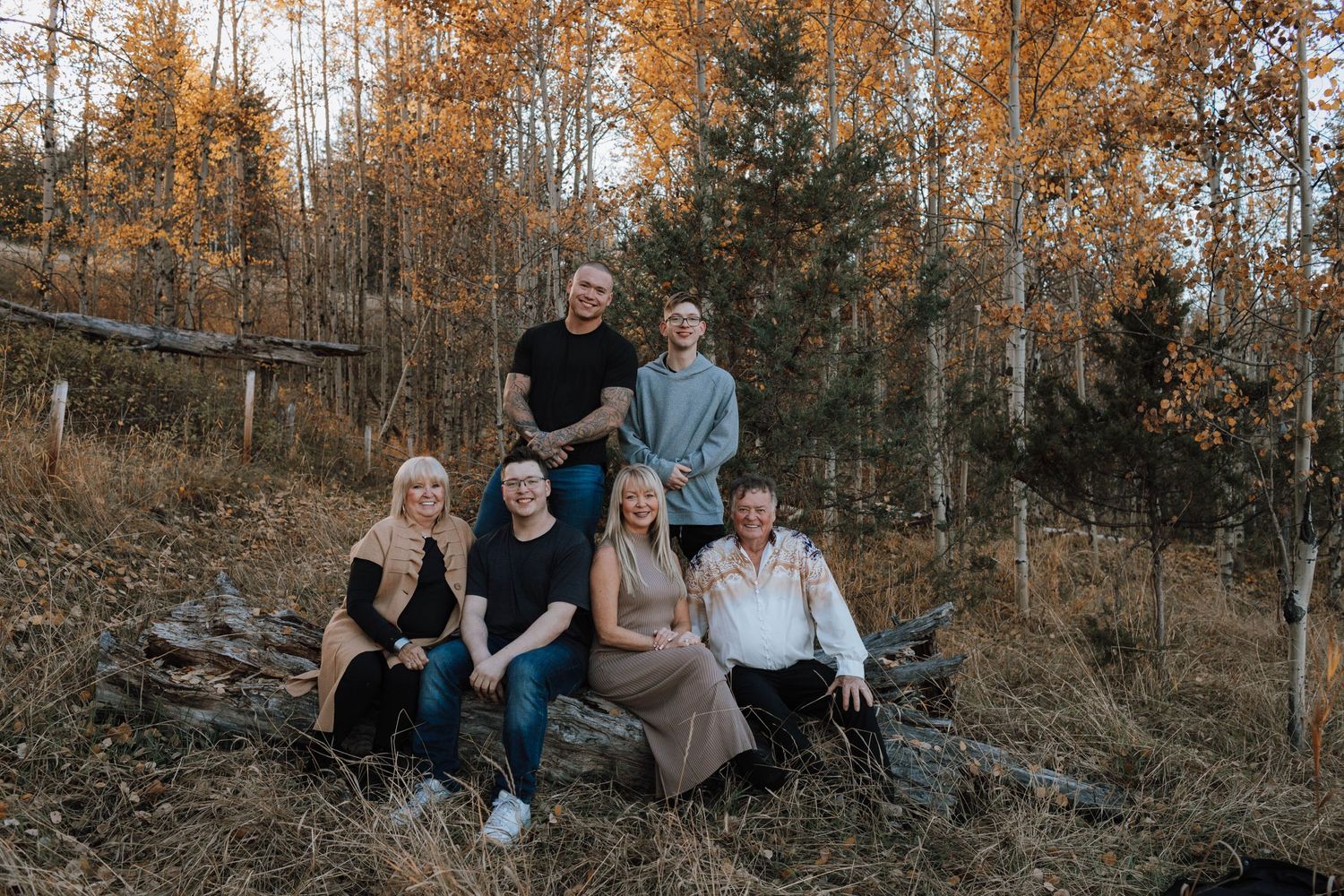 A group sits casually together on a hillside with autumn foliage in the background.