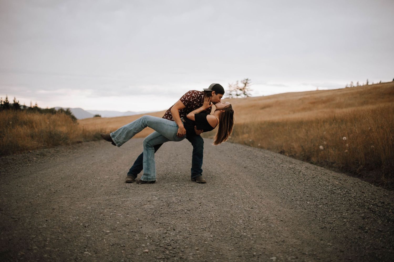 A romantic dip pose on a dirt road with rolling hills in the background.