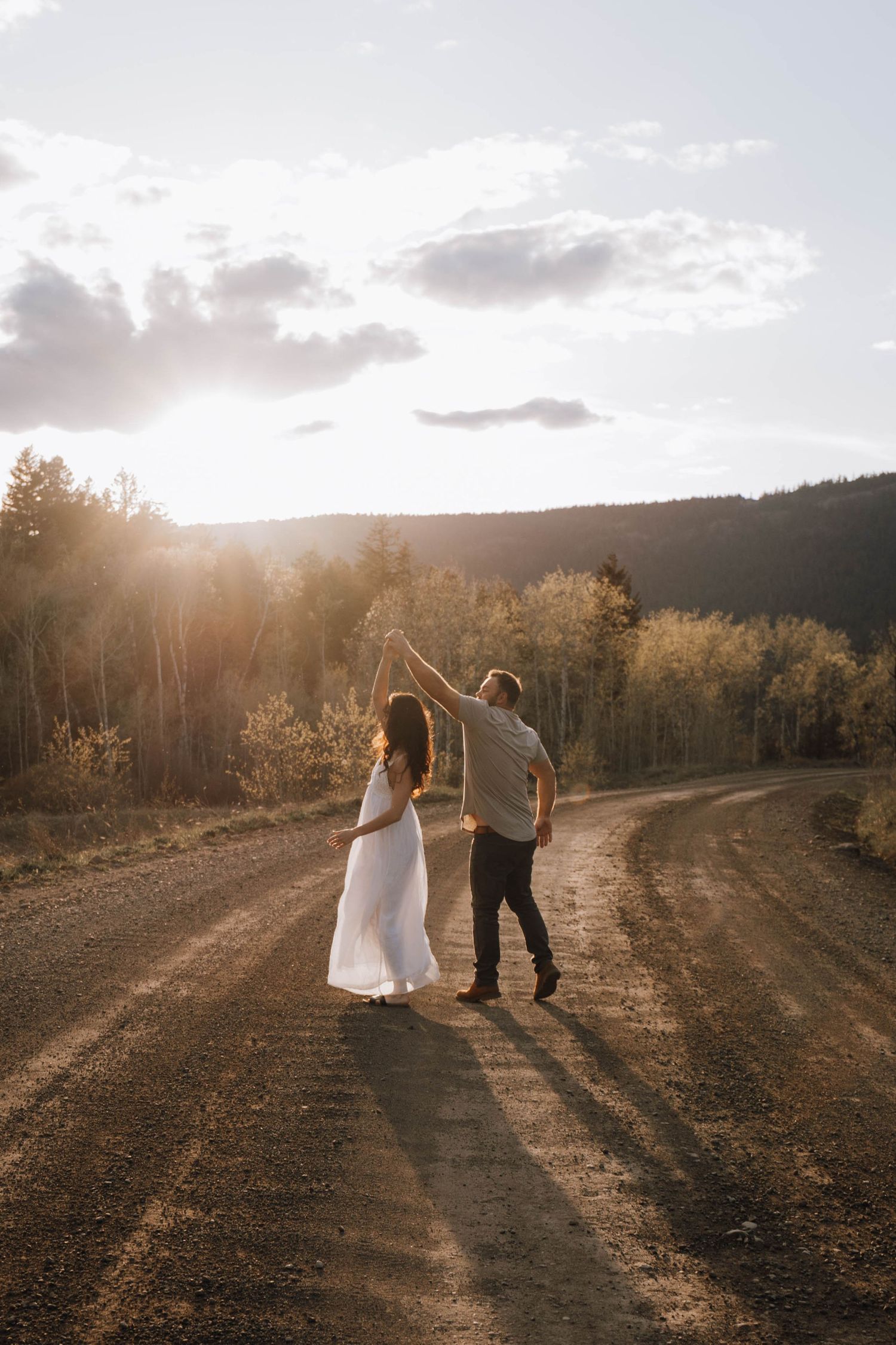 Couple dancing on a dirt road at golden sunset surrounded by autumn trees and rolling hills.