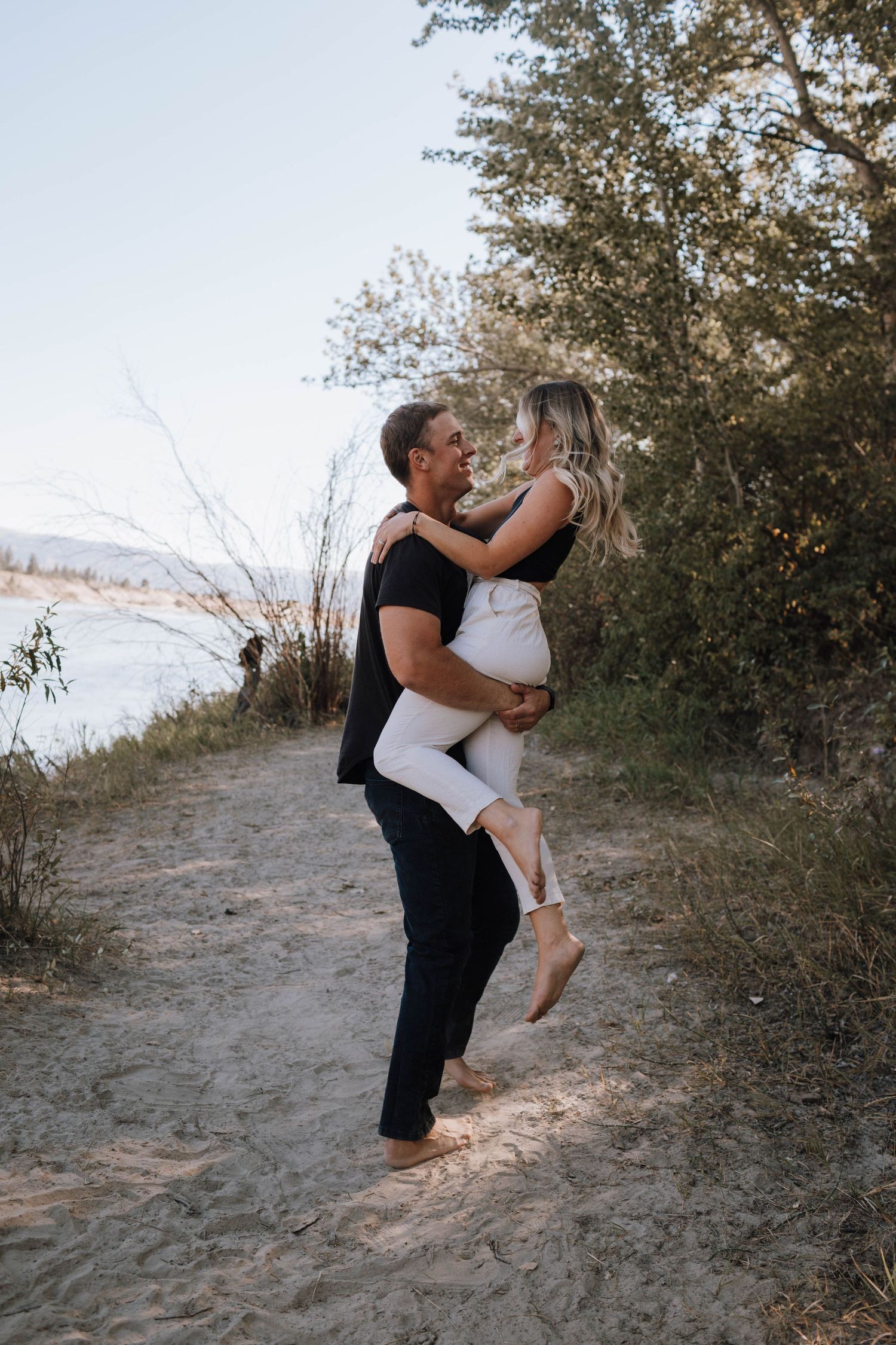 A couple embraces in a playful lift pose on a scenic waterfront trail.