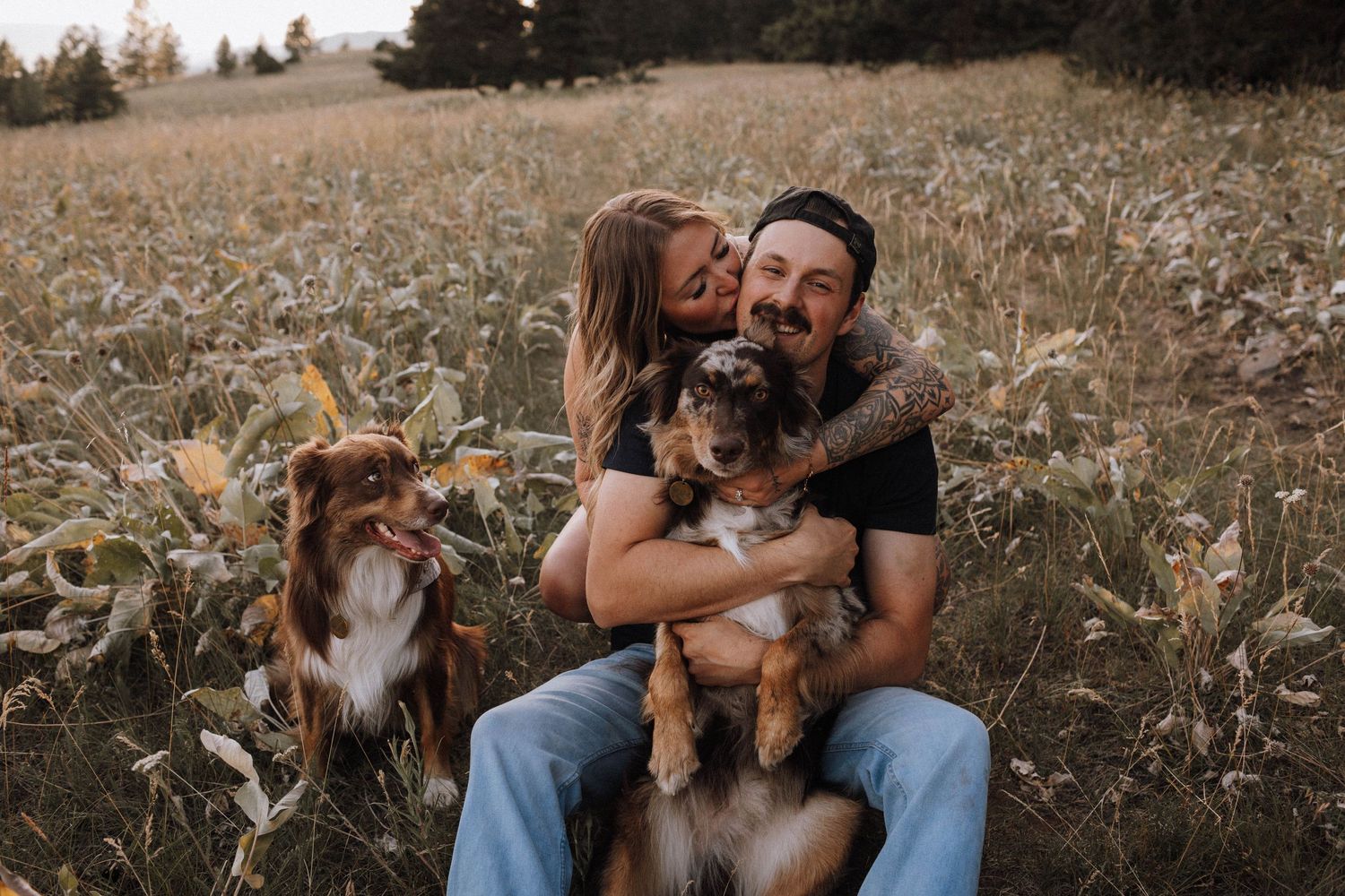 A couple sits together in a rustic field surrounded by tall grass during golden hour.