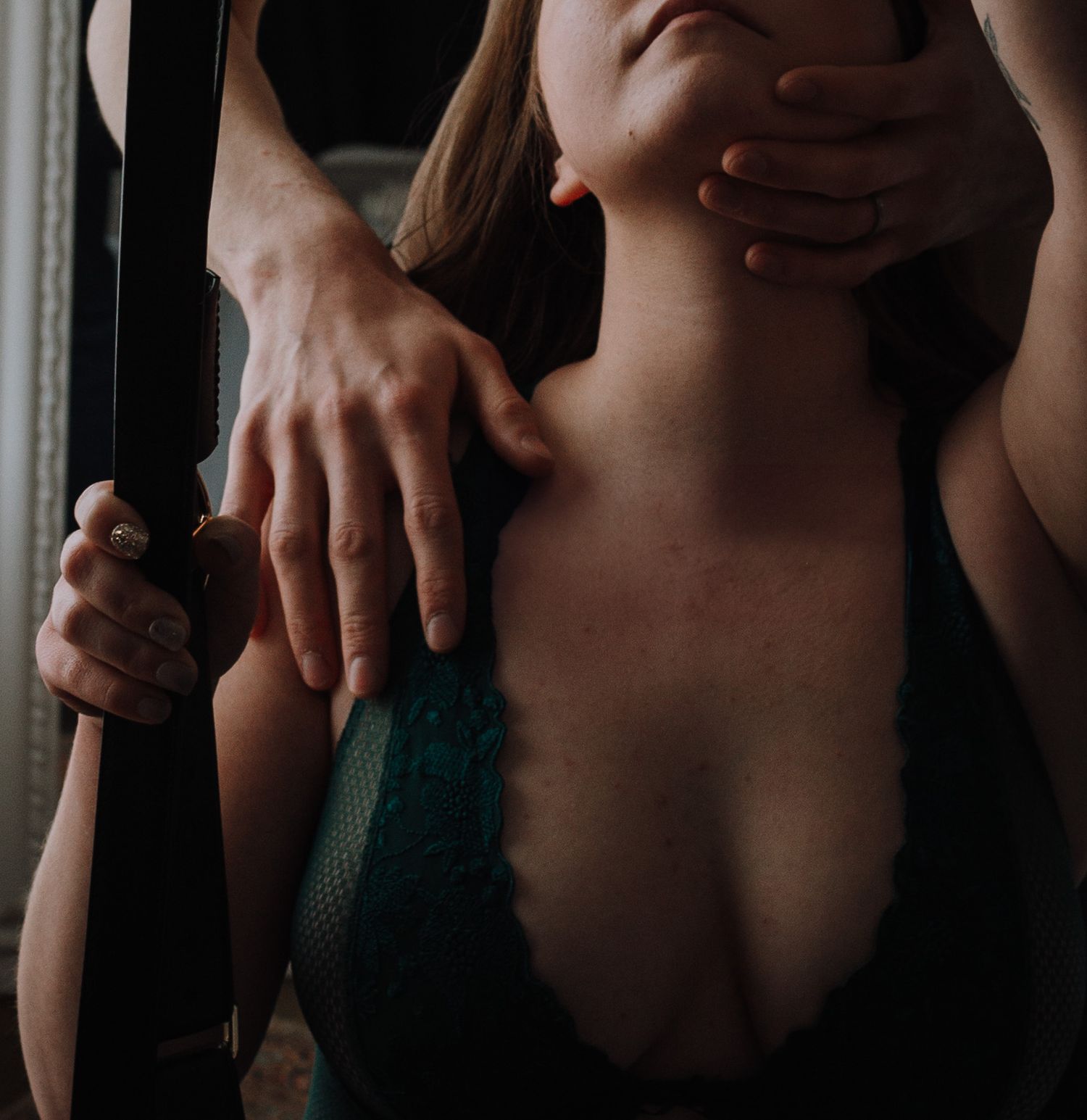 Close-up shot of hands gently holding shoulders in an intimate setting with dark atmosphere and green fabric.
