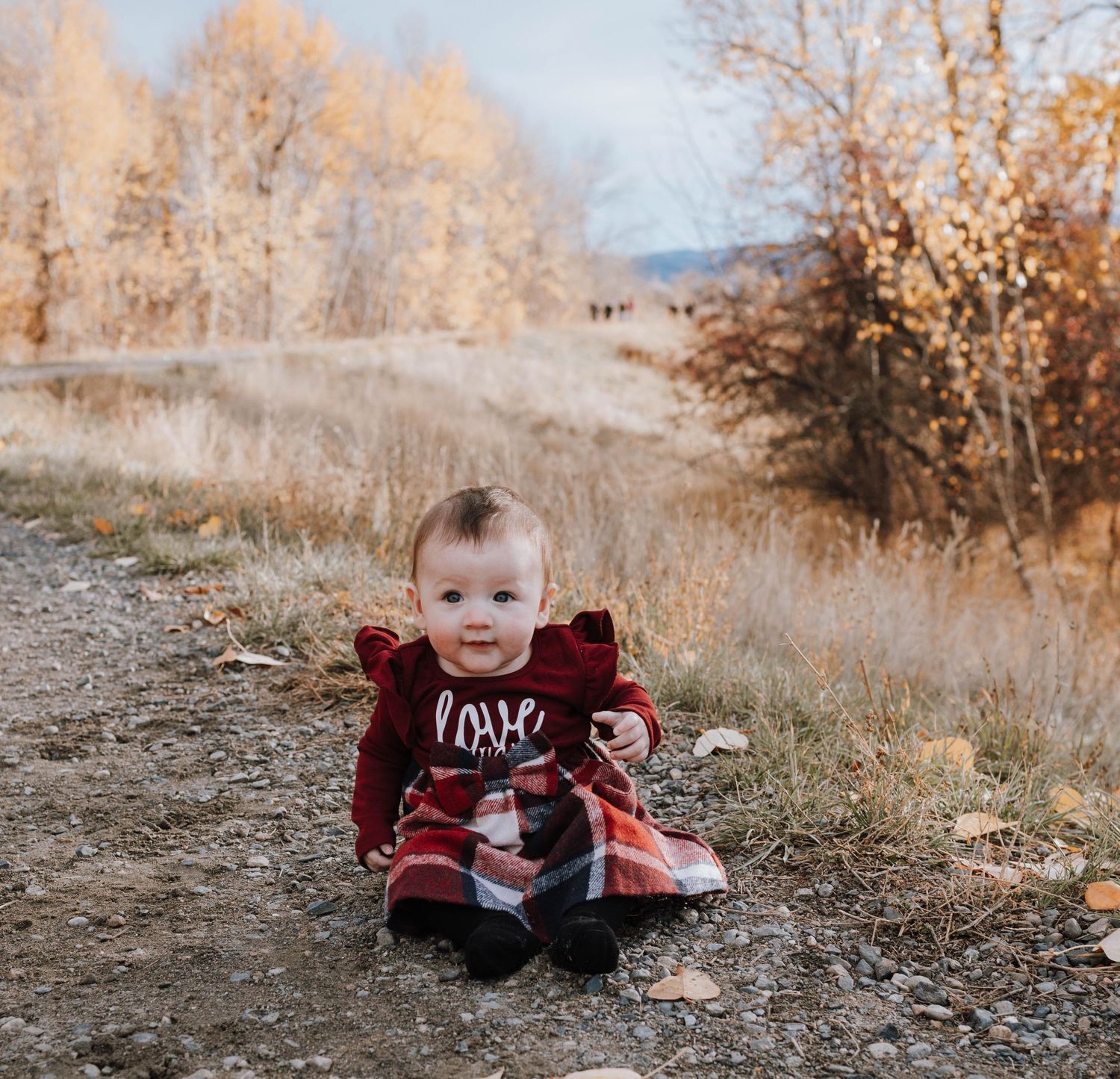 Small child wearing red love sweater sitting outdoors in fall setting.