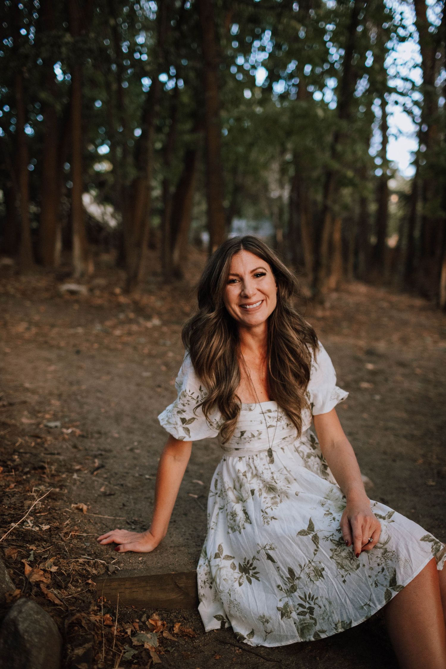 A white floral dress stands out against a wooded forest trail during golden hour.