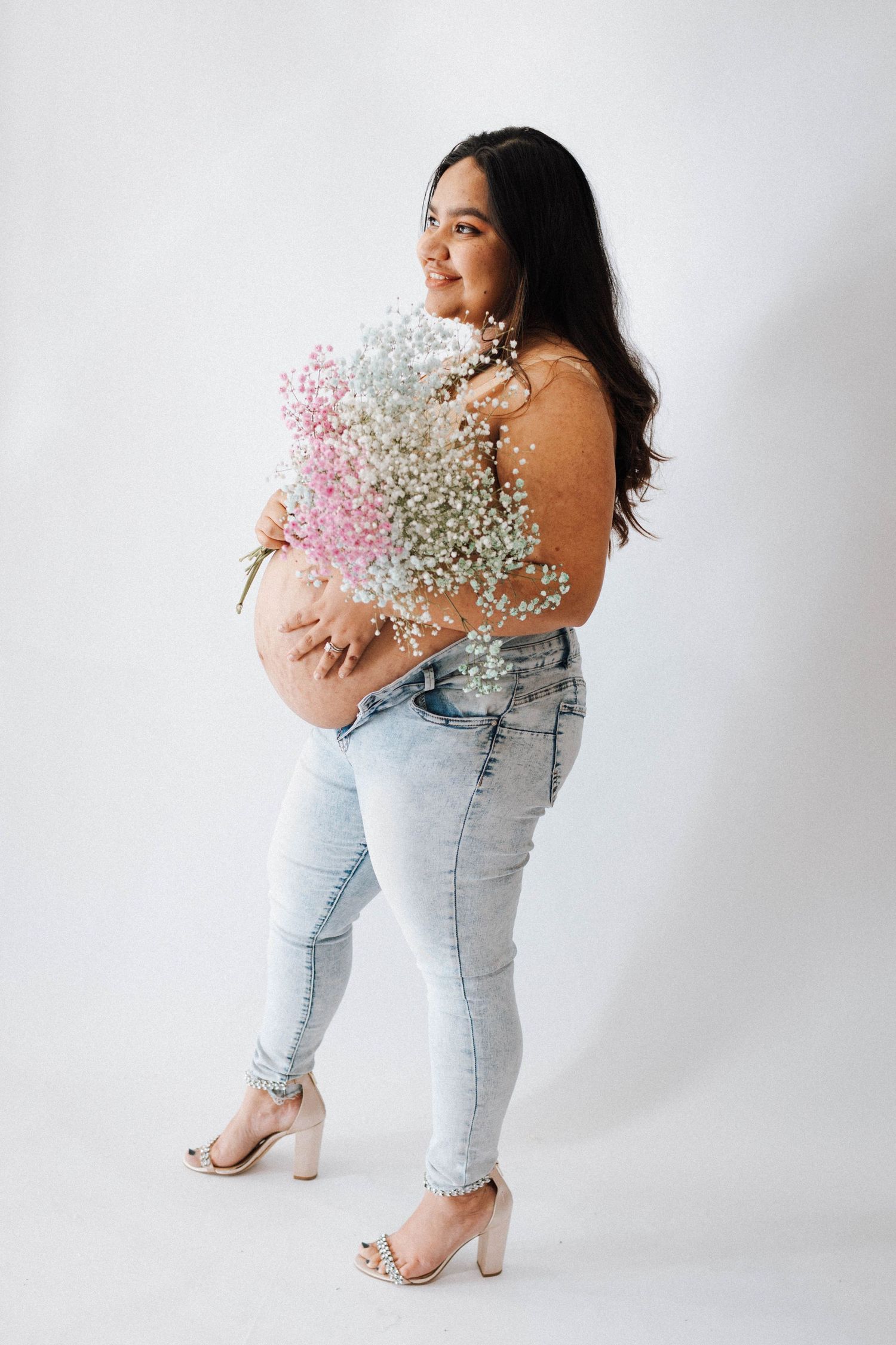 Person in light wash jeans and white top holding delicate pink and white baby's breath flowers against white background.
