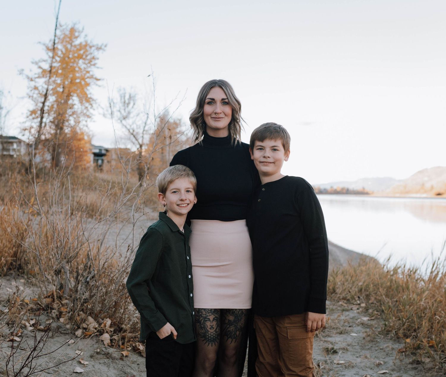 A family portrait taken outdoors against an autumn lakeside backdrop.