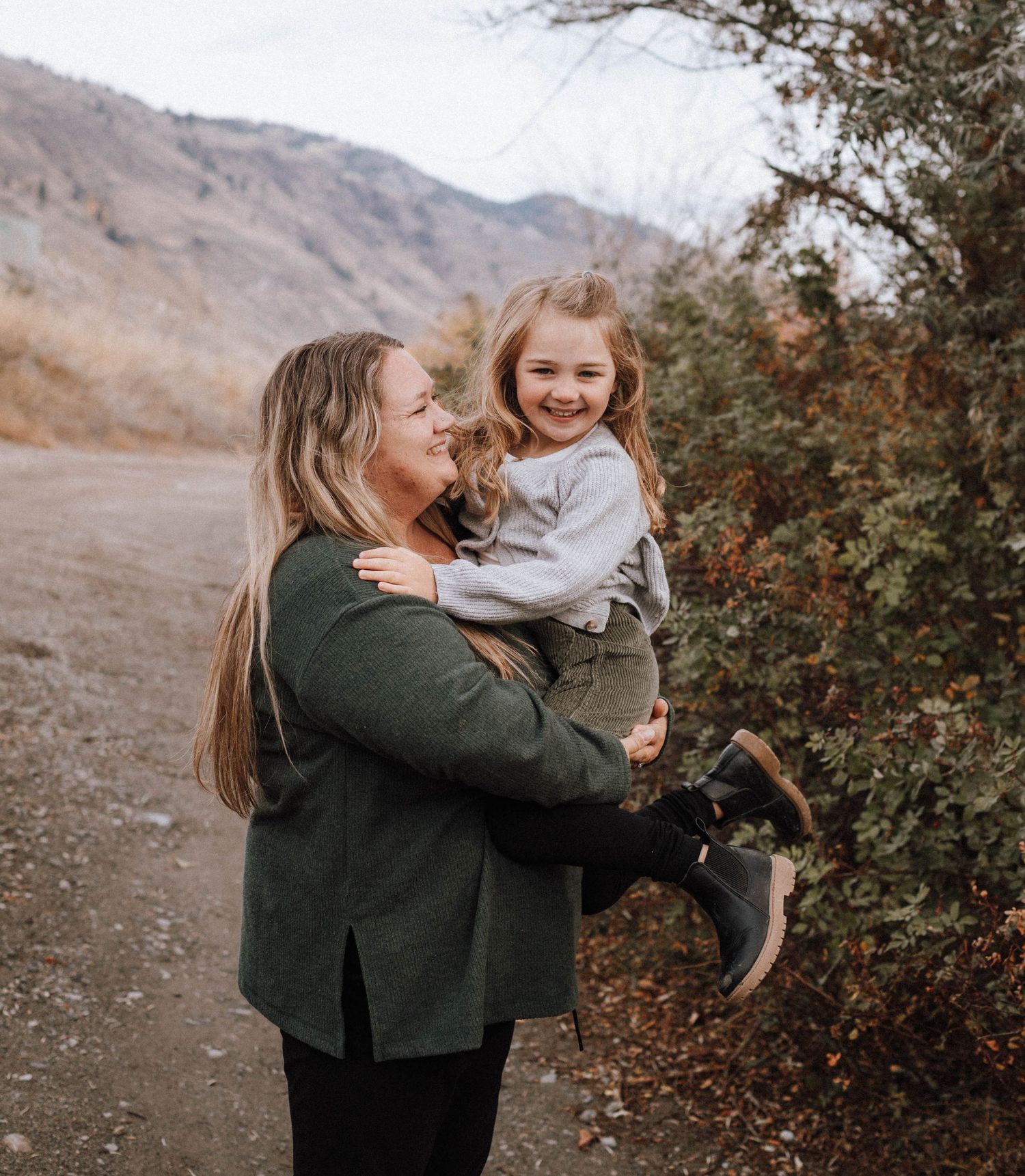 A joyful outdoor moment between parent and child against a mountain backdrop on a dirt path.