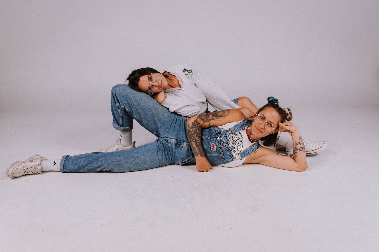 Two people in denim outfits lying on a white studio floor, posing casually for a photo shoot.